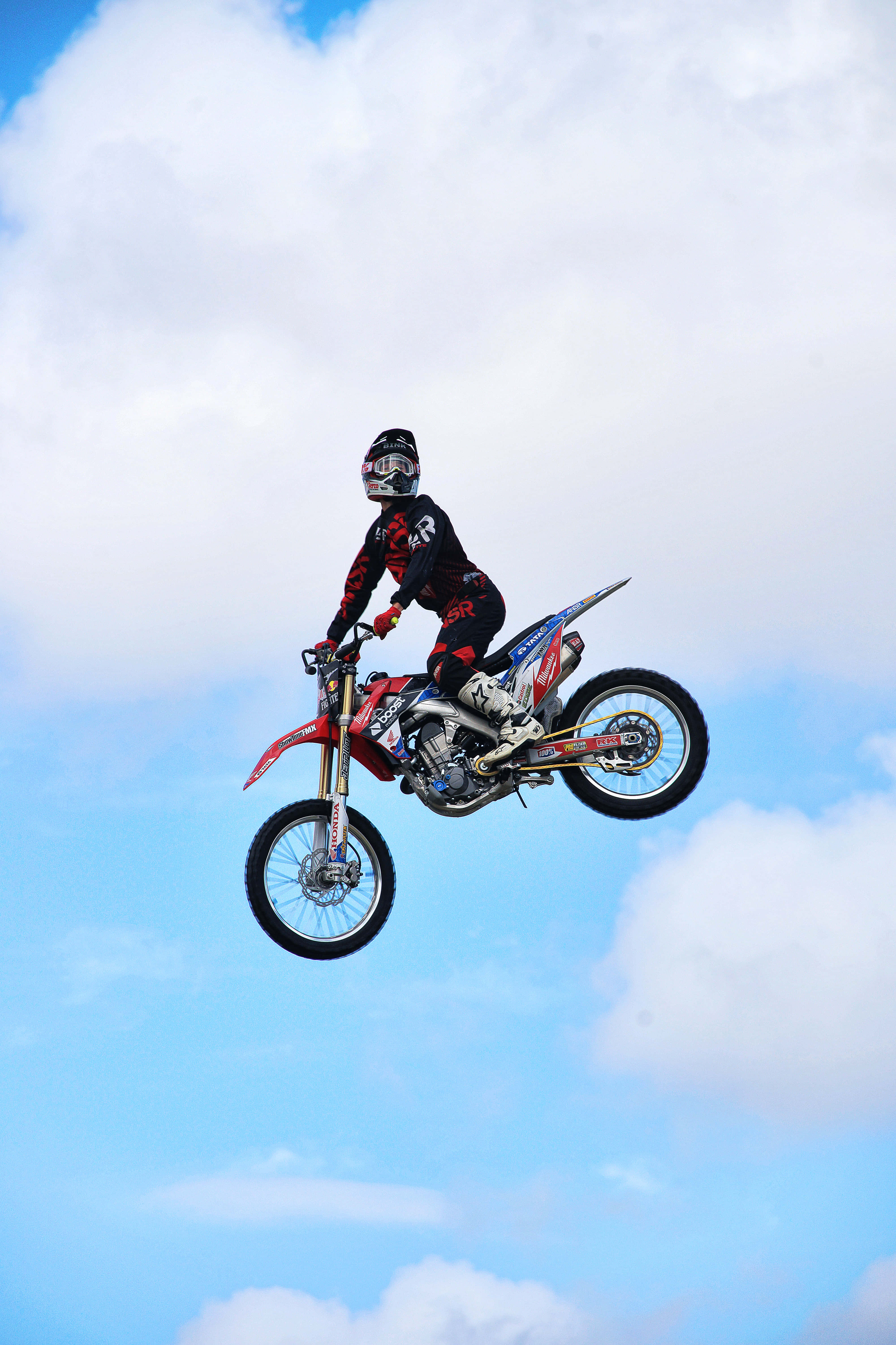 Dirtbike 桌布 壁紙 — 一名越野電單車手騎著紅色泥地電單車，在明亮的藍天白雲中翱翔。
