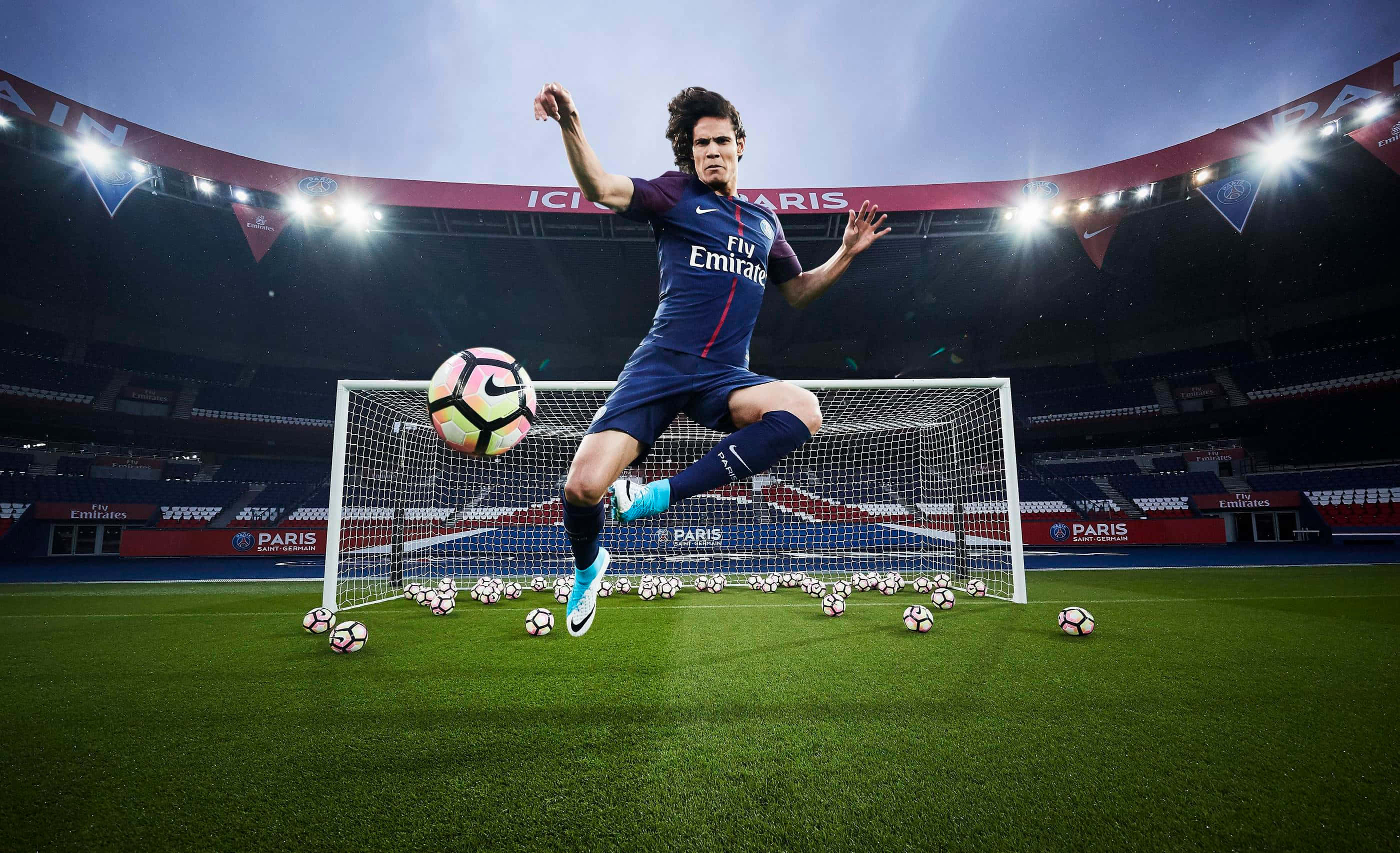 3d Sports 桌布 壁紙 — 一名足球員在半空中跳起，在球場燈光下，於一個被散落足球包圍的球門上方擊球。