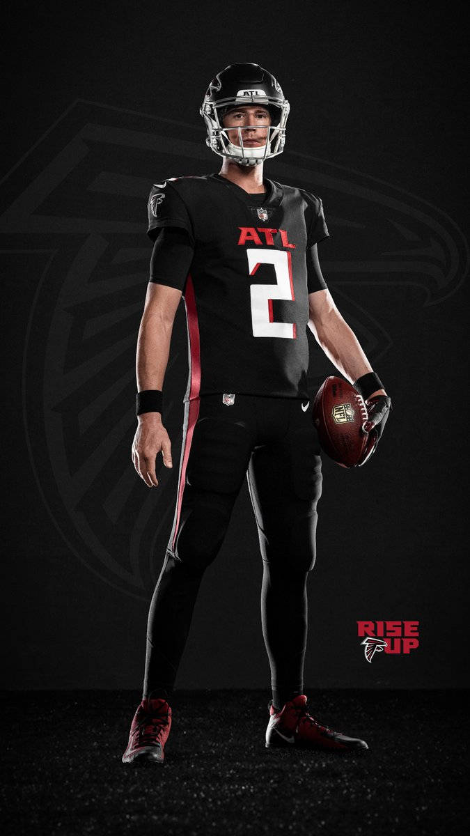 Matt Ryan 桌布 壁紙 — 一名身穿亞特蘭大獵鷹隊裝備的足球員自信地站在深色背景前，手持球，背景有球隊標誌。