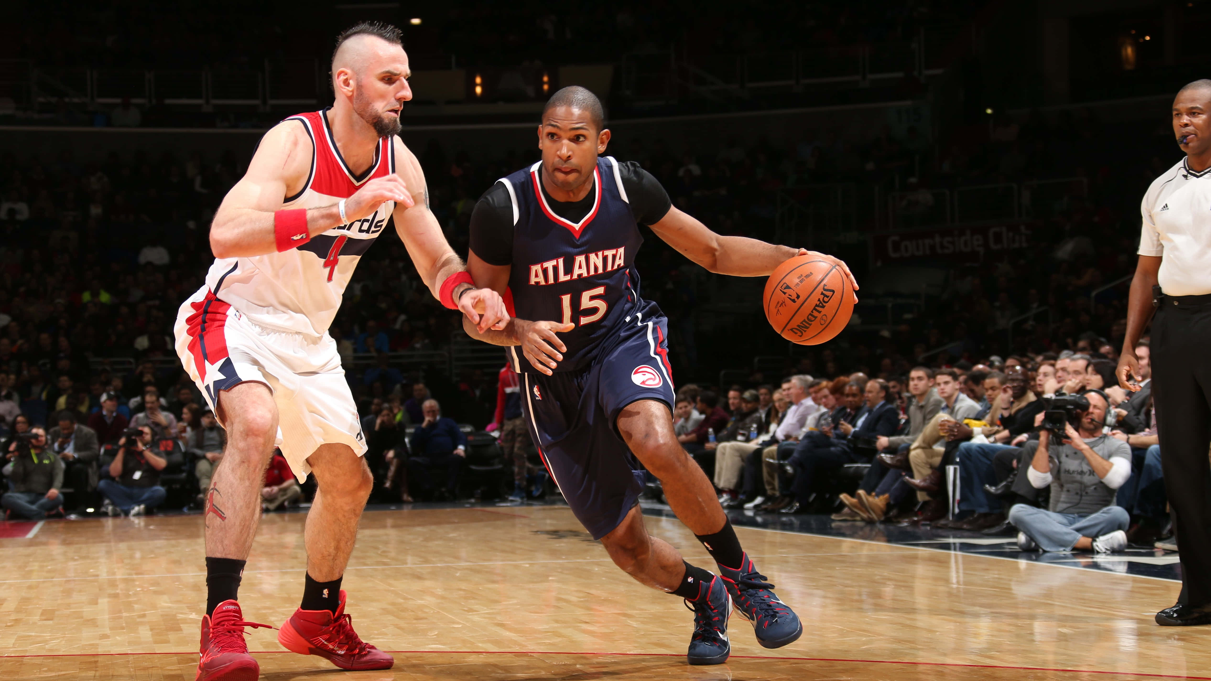 Al Horford 桌布 壁紙 — 一名身穿亞特蘭大球衣的籃球運動員在場館燈光下的高風險比賽中運球越過華盛頓巫師隊的防守球員。