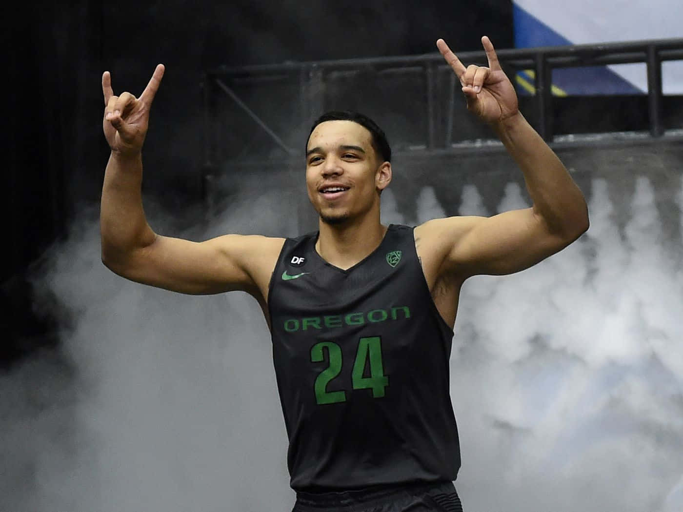 Dillon Brooks 桌布 壁紙 — 一名身穿俄勒岡球衣的籃球運動員在球場煙霧中做出搖滾手勢慶祝。