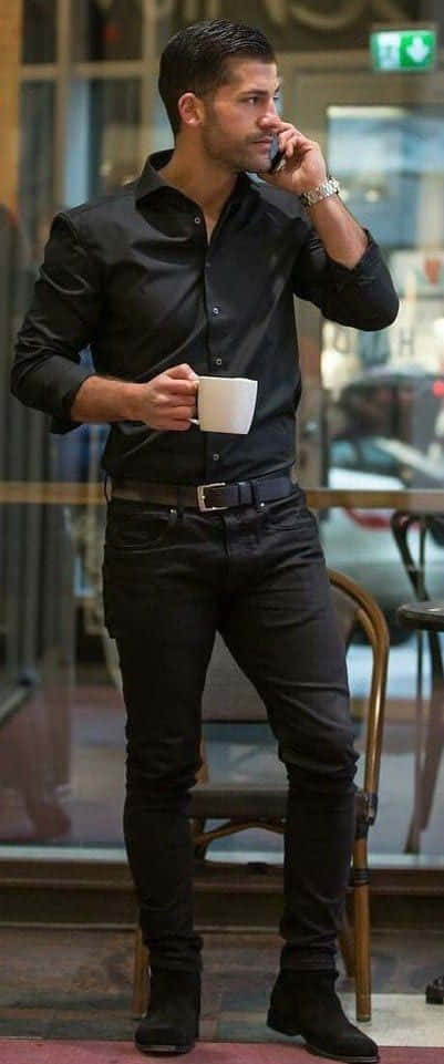 Black Clothing 桌布 壁紙 — 一名身穿全黑服飾的男子站在咖啡館窗前，手持白色馬克杯正在講電話。