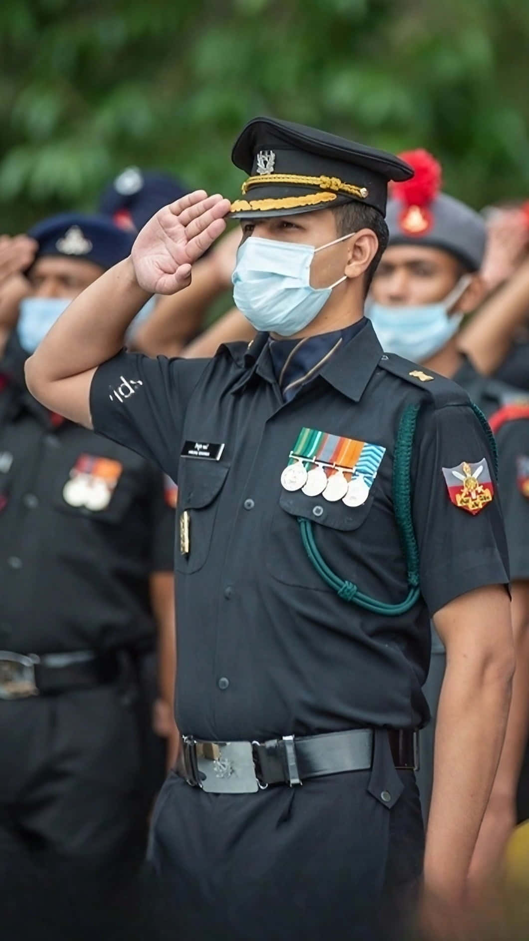 Indian Army 桌布 壁紙 — 一名身穿制服的軍官在戶外正式儀式上戴著口罩敬禮，背景有模糊的同事。