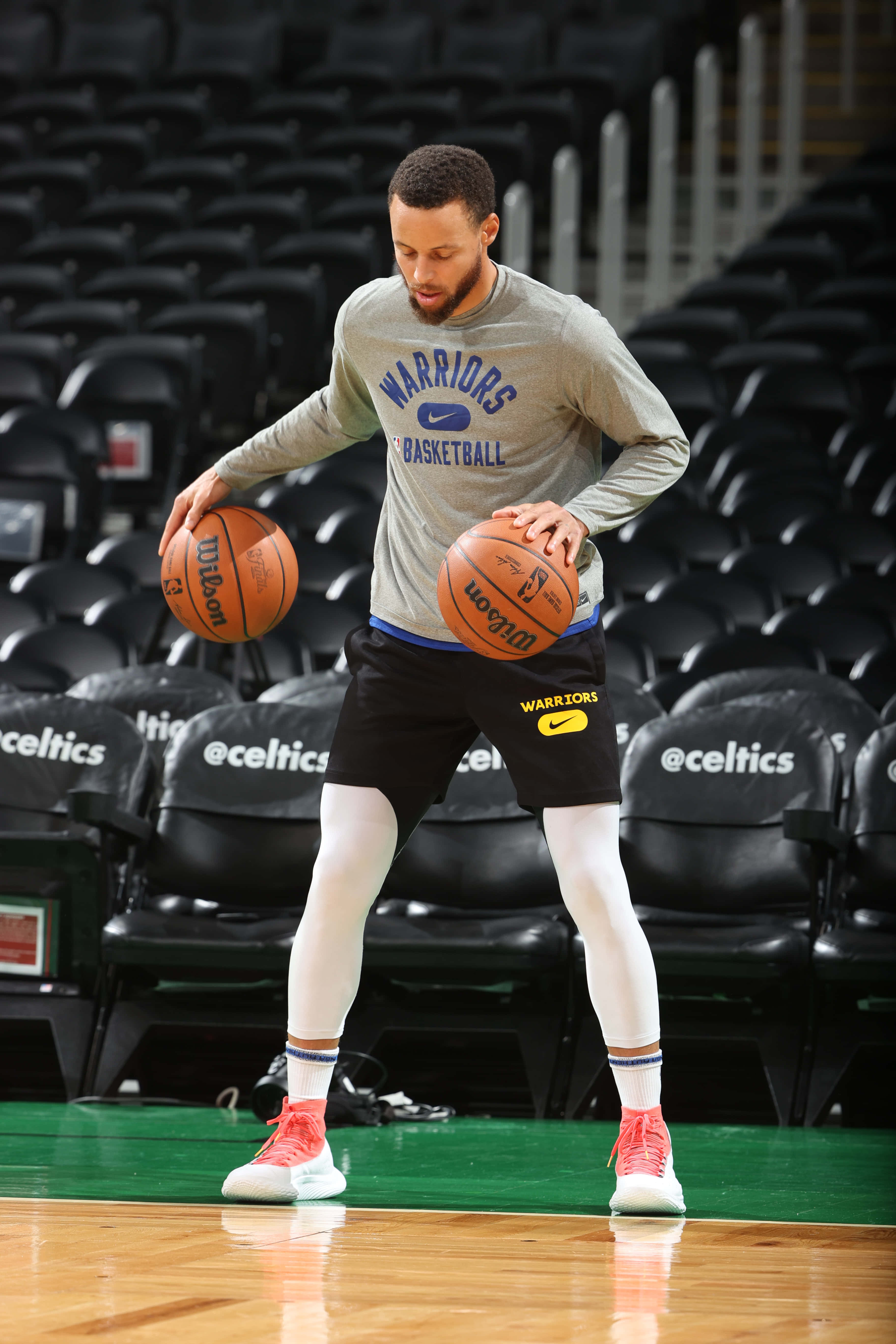 steph curry 桌布 壁紙 — 一名身穿勇士隊裝備的籃球運動員在球場上運兩個球，身後是空的塞爾特人座位。