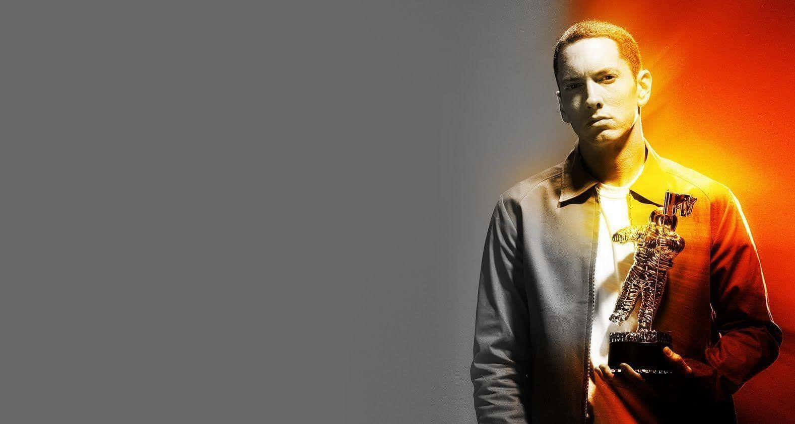 Eminem 桌布 壁紙 — 一名身穿外套的男子在強烈的灰色和火橙色背景下手持MTV獎項。