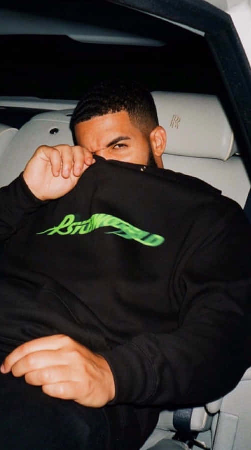Drake - Feel No Ways 壁紙 — 一名身穿帶有綠色文字的黑色連帽衫的男子坐在豪華車內，拉起帽子遮住臉部。