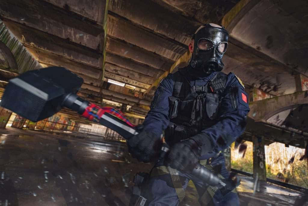 Rainbow Six Siege Sledge 桌布 壁紙 — 一名身穿戰術裝備和防毒面具的人，在黃昏時分於佈滿塗鴉的橋下揮舞著大錘。