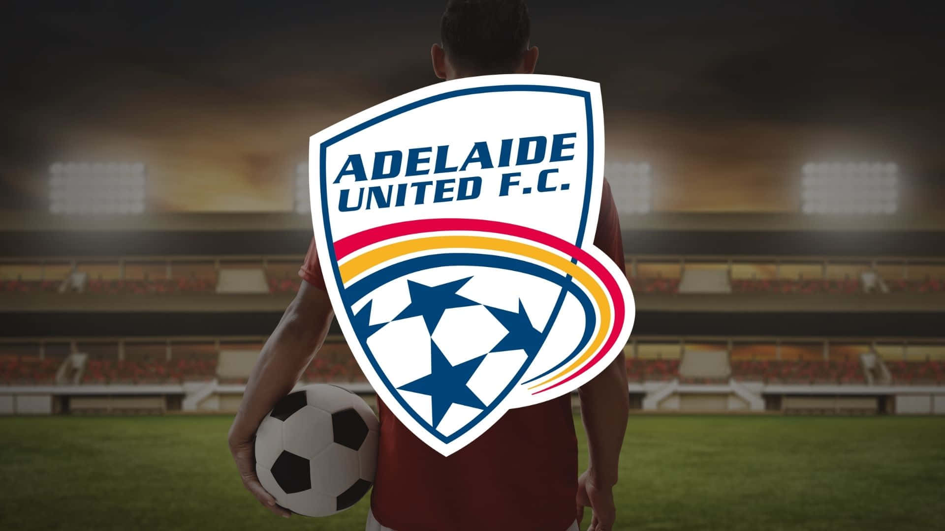 Adelaide United 桌布 壁紙 — 一名身穿栗色球衣的足球員站在草地上，背景中體育場的燈光閃爍，手持足球。