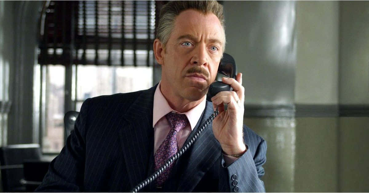 J Jonah Jameson 桌布 壁紙 — 一名身穿條紋西裝的男子在現代辦公室裏，表情嚴肅地將電話貼在耳邊。