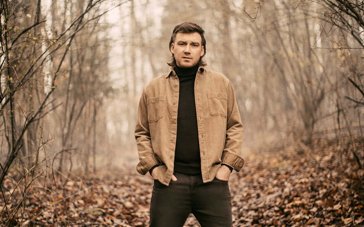 Morgan Wallen 桌布 壁紙 — 一名身穿棕色外套的男子平靜地站在霧氣瀰漫的秋林中，周圍是光禿的樹木和落葉。