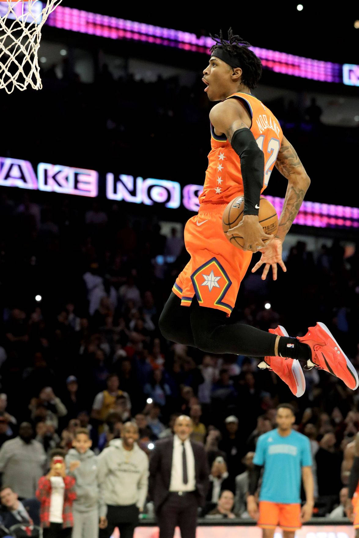 Ja Morant 入樽 桌布 壁紙 — 一名身穿橙色球衣的籃球運動員在擠滿觀眾的場館中高高躍起，將球灌入上方的籃框。