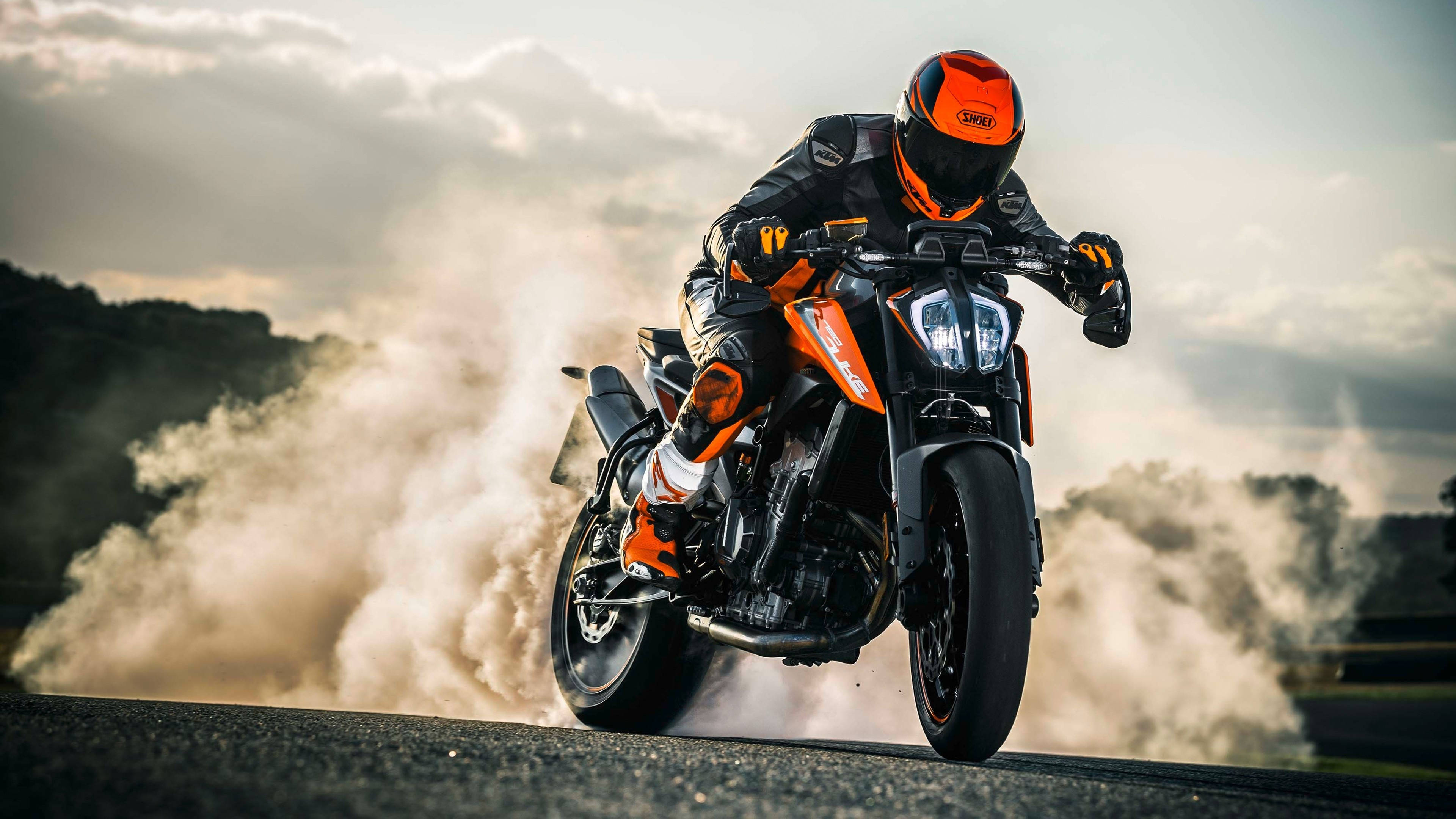 ktm rc 200 桌布 壁紙 — 一名身穿橙色裝備的電單車手在黑色和橙色的KTM電單車上傾斜入彎，在蜿蜒的道路上揚起灰塵。