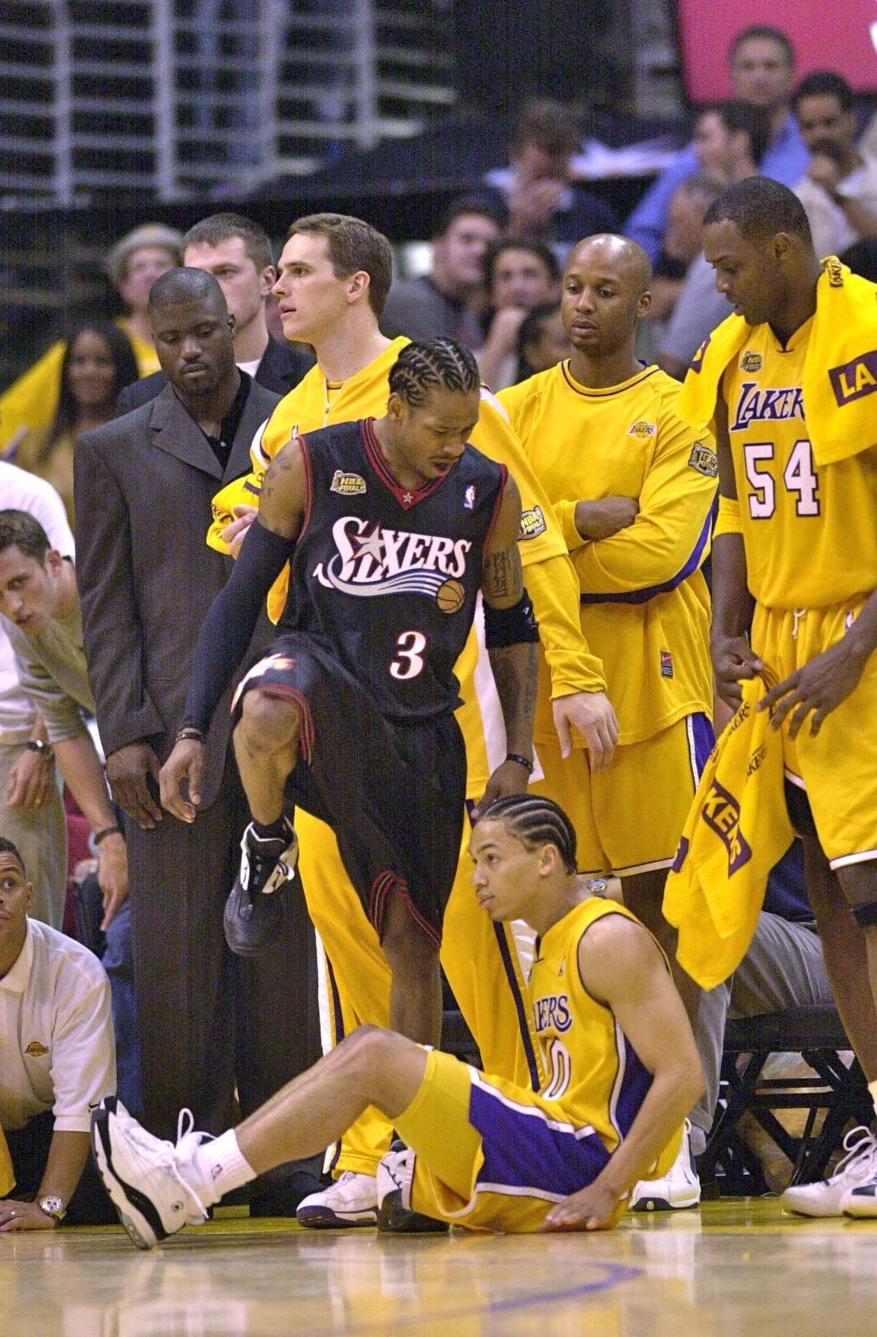 NBA 桌布 壁紙 — 一名身穿深色Sixers球衣的籃球運動員站在光滑球場上倒地的Lakers球員上方，隊友和教練們專注地觀看。