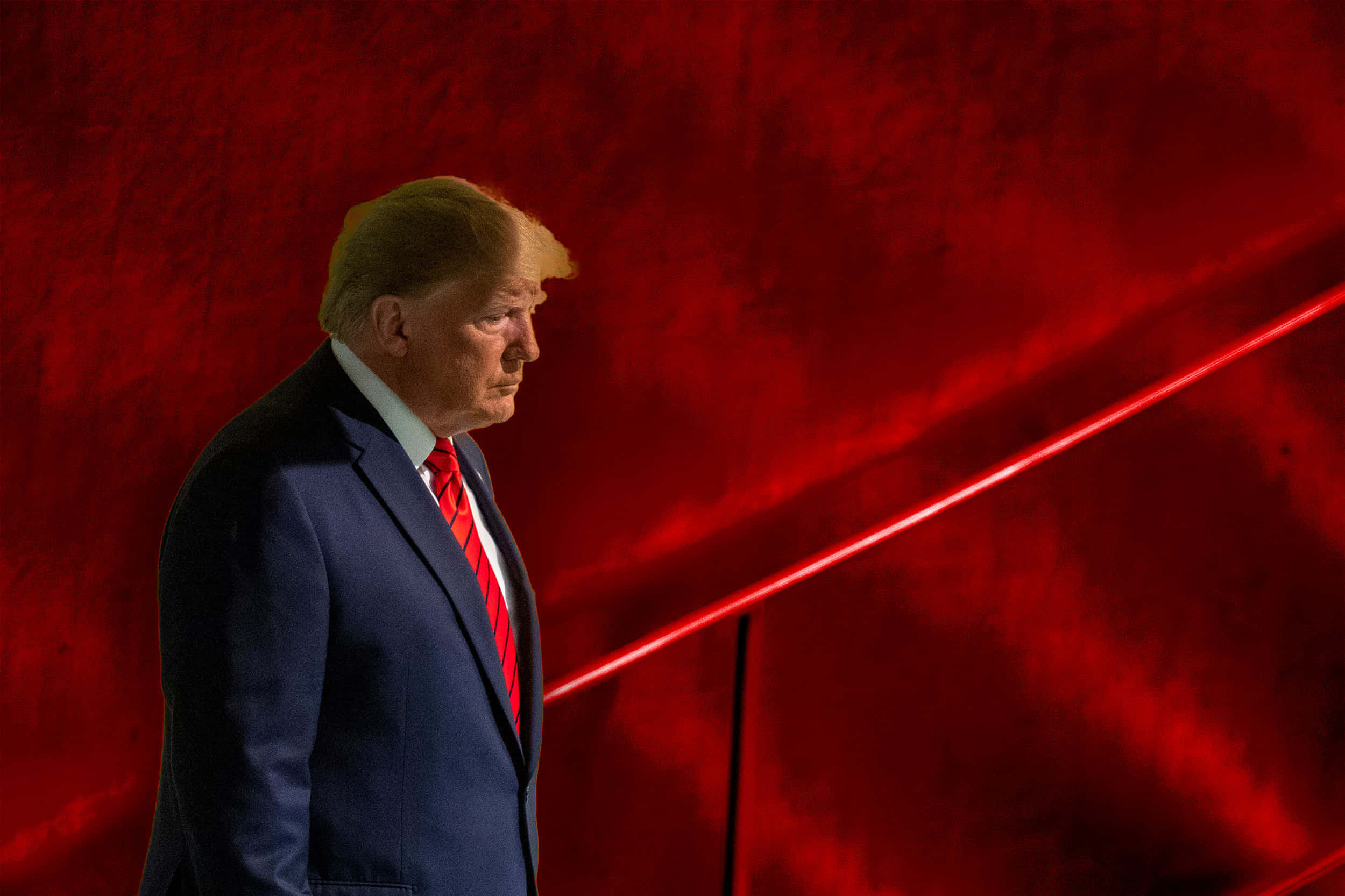 trump 桌布 壁紙 — 一名身穿深色西裝和紅色領帶的男子，側面站在帶有斜向光紋的紋理深紅色背景前。
