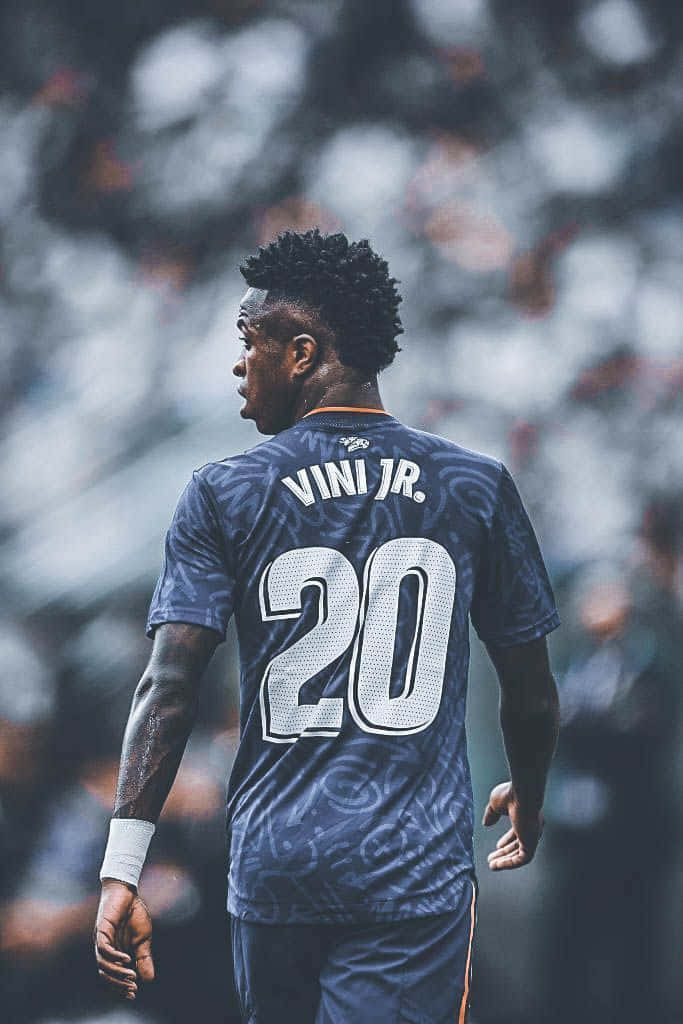  壁紙 — 一名身穿深藍色球衣、印有「VINI JR.」和20號的足球員在模糊的球場上背對鏡頭走開。