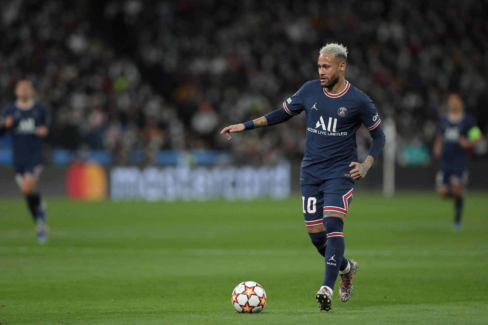 Neymar 桌布 壁紙 — 一名身穿深藍色球衣的足球運動員在體育場燈光下，於充滿活力的綠色球場上盤帶一顆星形圖案的足球。