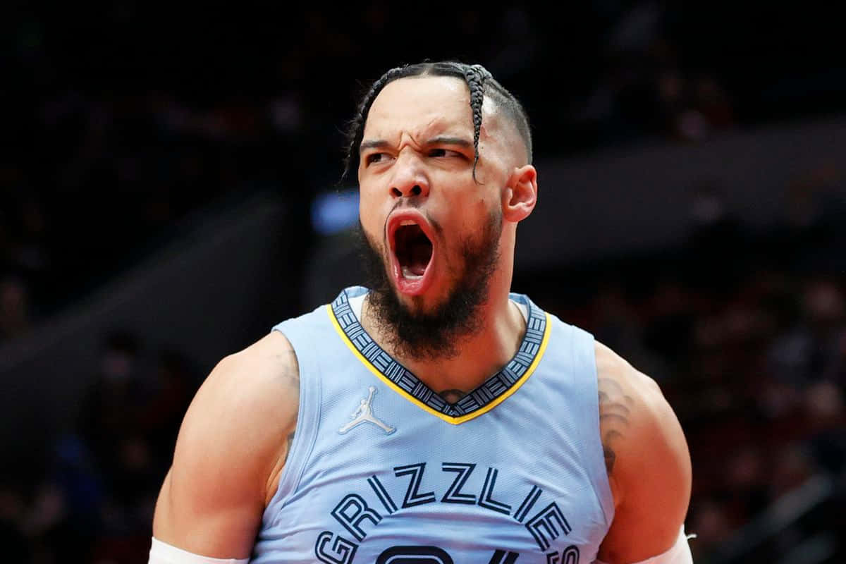 Dillon Brooks 桌布 壁紙 — 一名身穿淺藍色灰熊隊球衣的籃球運動員在場館燈光下比賽時，充滿激情地咆哮。