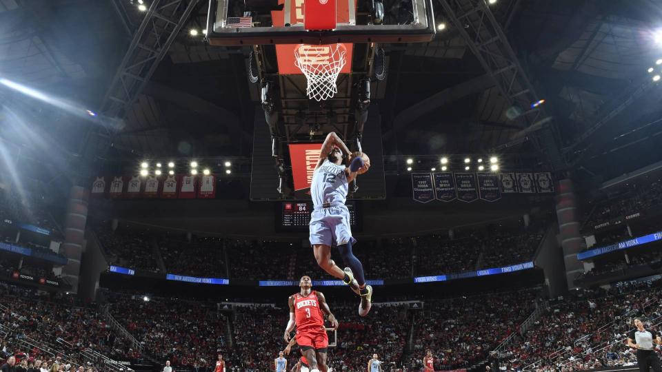 Houston Rockets 桌布 壁紙 — 一名身穿淺藍色球衣的籃球運動員在空中飛翔進行入樽，而一名紅色球衣的防守球員在擠滿觀眾的場館下方觀看。