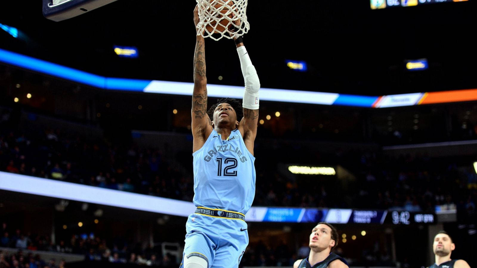 Grizzlies 桌布 壁紙 — 一名身穿淺藍色球衣的籃球運動員在夜間比賽中，在明亮的場館燈光下強力灌籃。