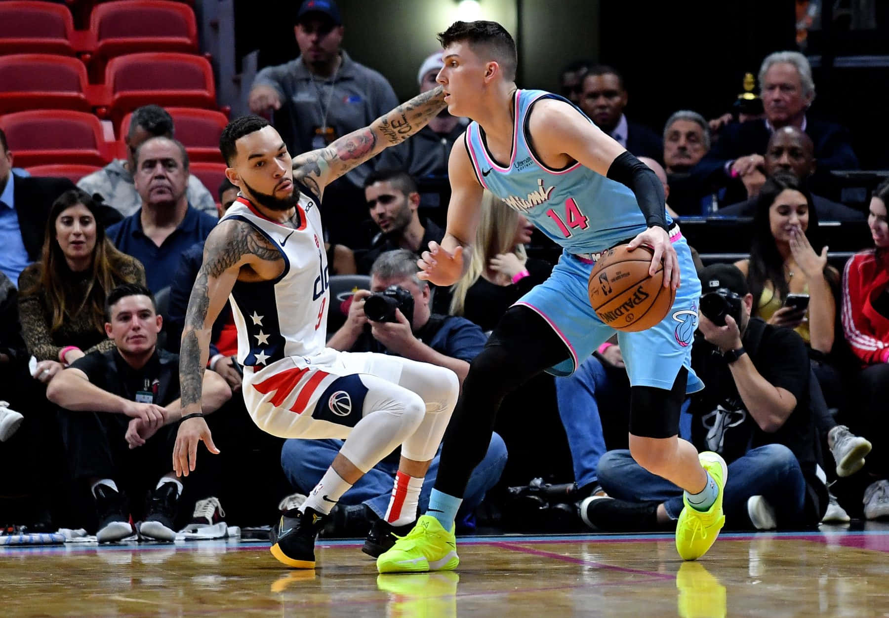 Tyler Herro 桌布 壁紙 — 一名身穿淺藍色球衣的籃球運動員正在運球，同時被一名身穿白色球衣、雙臂有紋身的對手緊密防守。