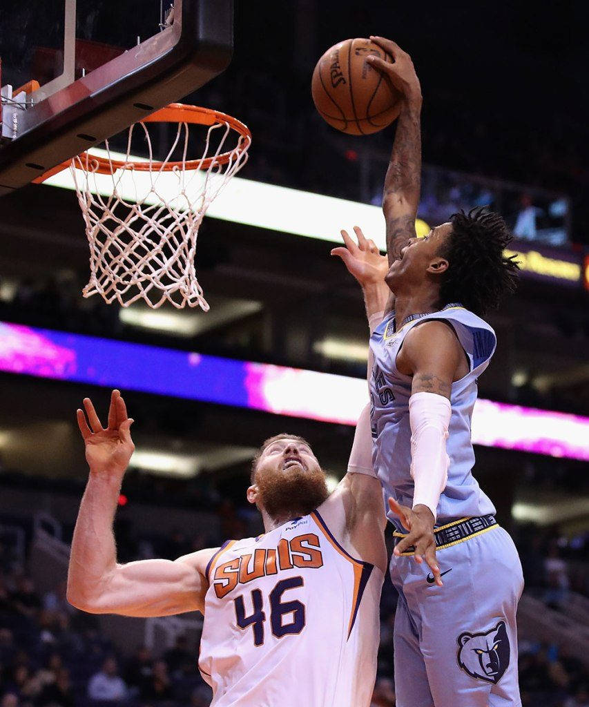 Ja Morant 入樽 桌布 壁紙 — 一名身穿淺藍色球衣的籃球運動員跳起入樽，而一名身穿白色Suns球衣的防守球員試圖封阻。