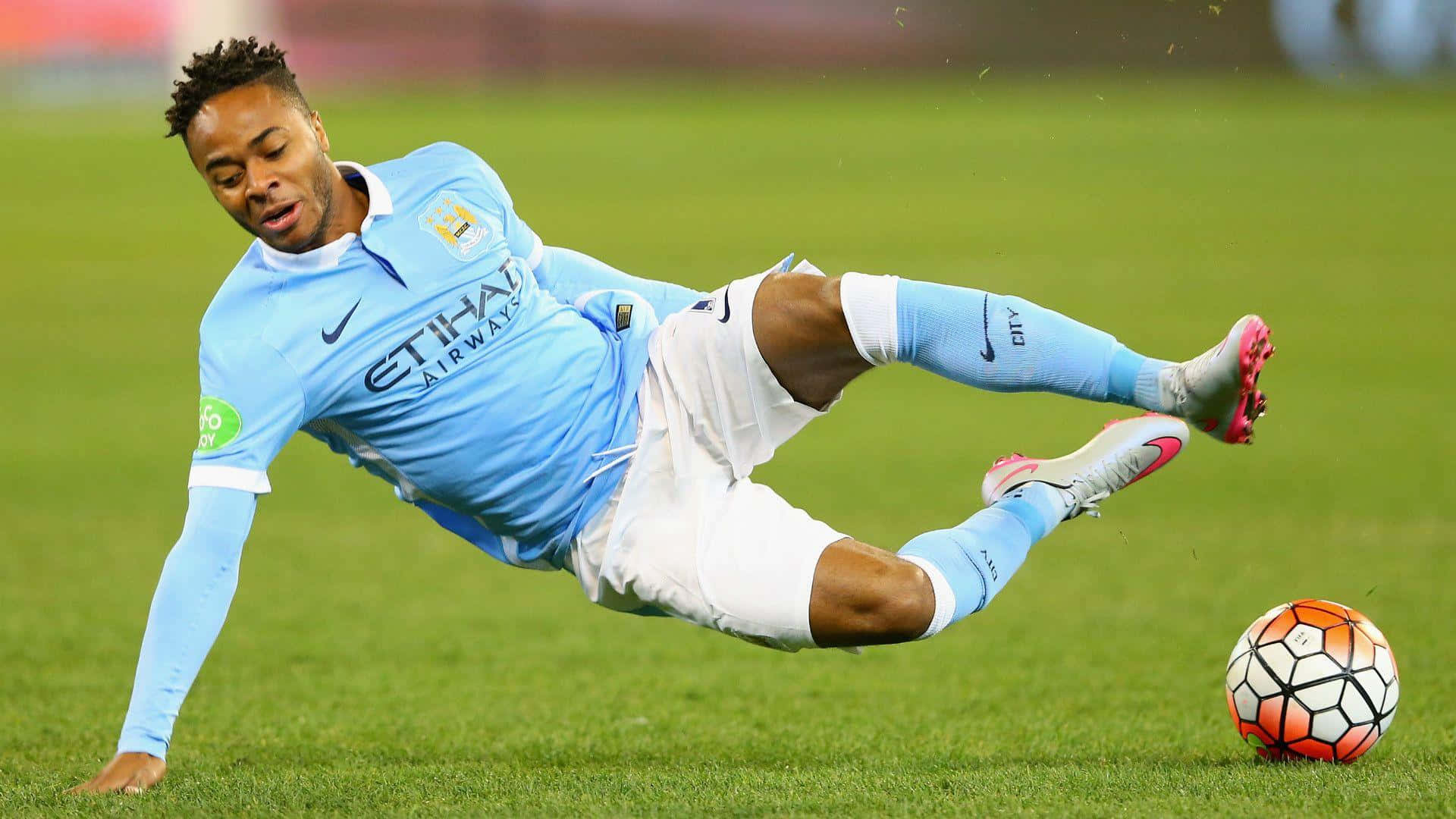 Sterling 桌布 壁紙 — 一名身穿淺藍色球衣的足球員動態地飛撲過充滿活力的綠色球場，搶奪一個色彩繽紛的球。