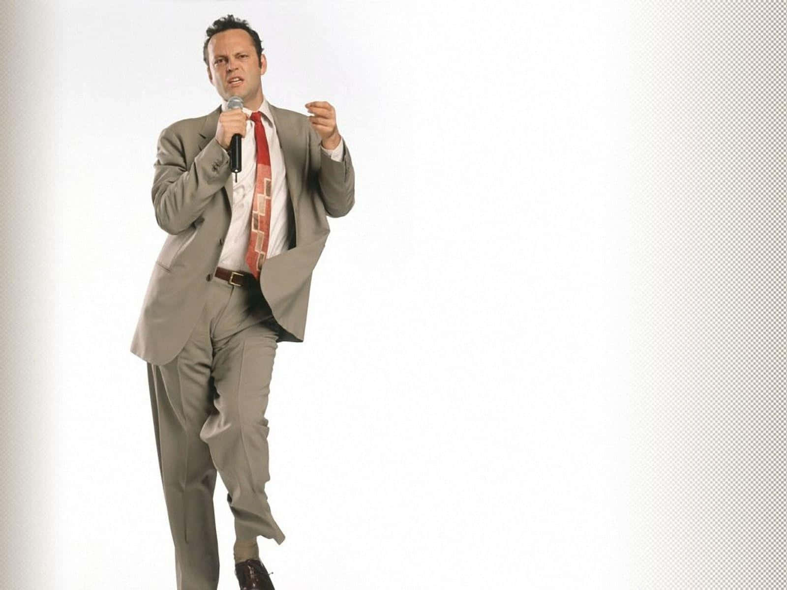 Vince Vaughn 桌布 壁紙 — 一名身穿灰色西裝、打紅色領帶的男子，在純白的工作室背景前，對著麥克風深情演唱。