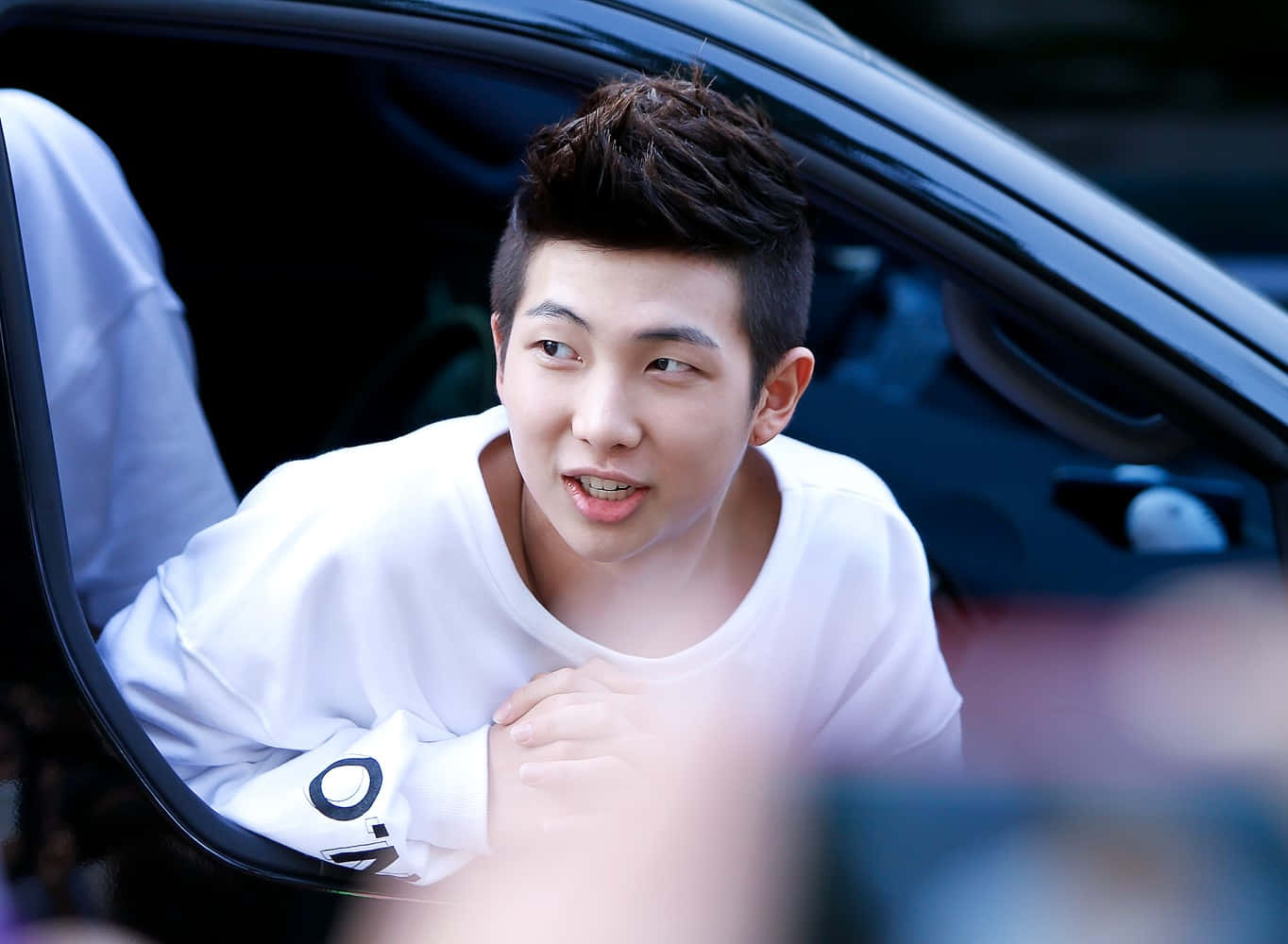 Bts Rap Monster 桌布 壁紙 — 一名身穿白恤衫的年輕男子，帶著頑皮的表情從車窗探出頭來。