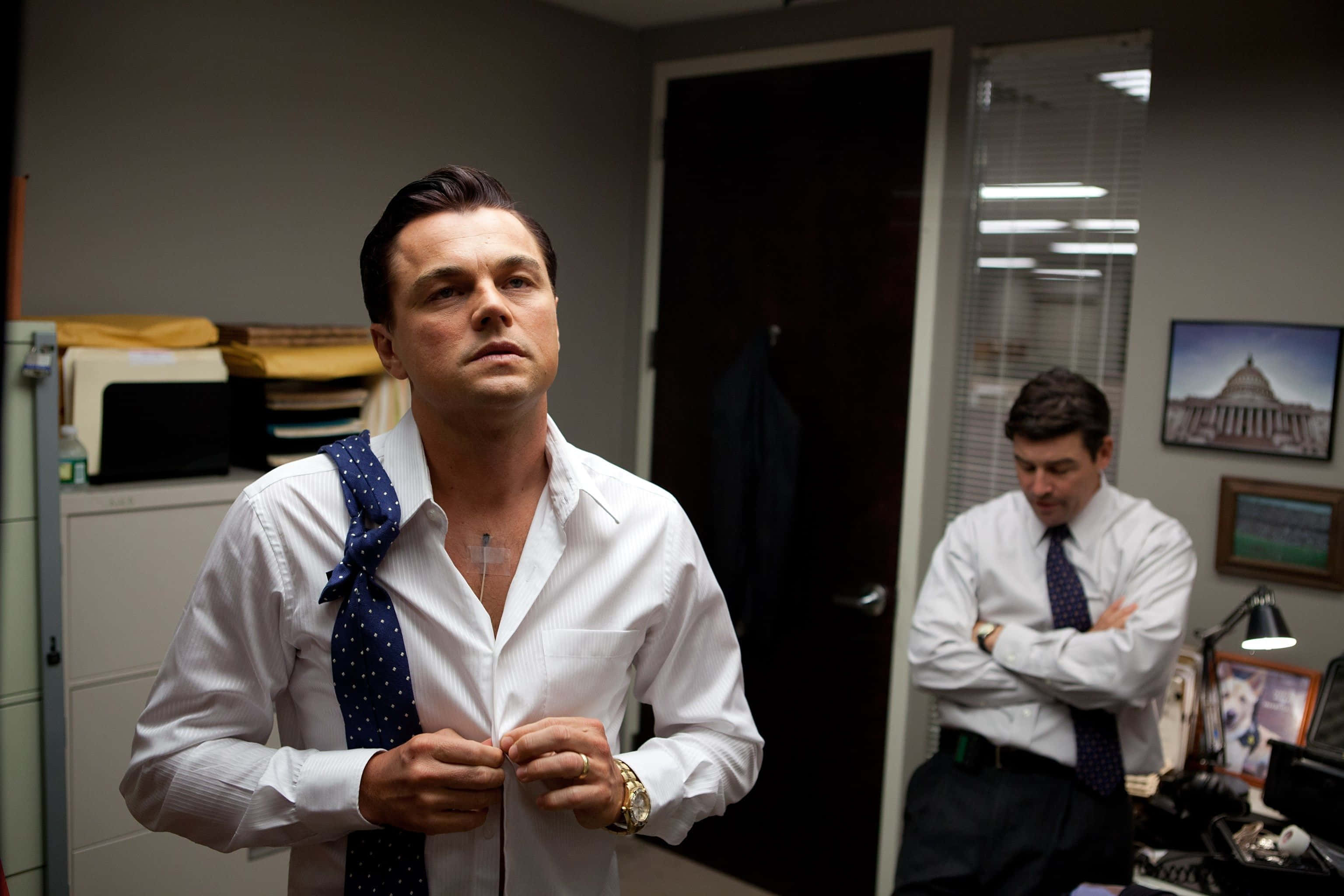 Wolf Of Wall Street 桌布 壁紙 — 一名身穿白恤衫的男子正在扣鈕，另一名男子雙手交叉站立在辦公室背景中。