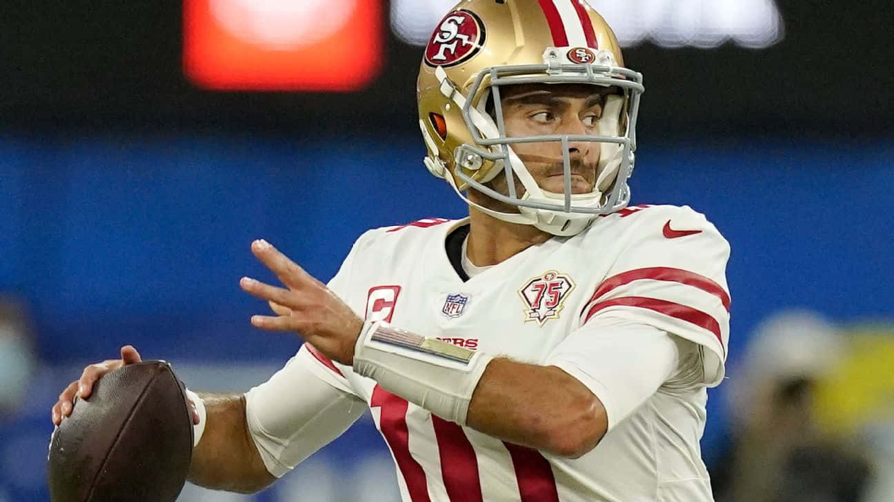 Jimmy Garoppolo 桌布 壁紙 — 一名身穿白色和紅色球衣的三藩市四九人四分衛在夜間比賽中，在球場燈光下準備擲出橄欖球。