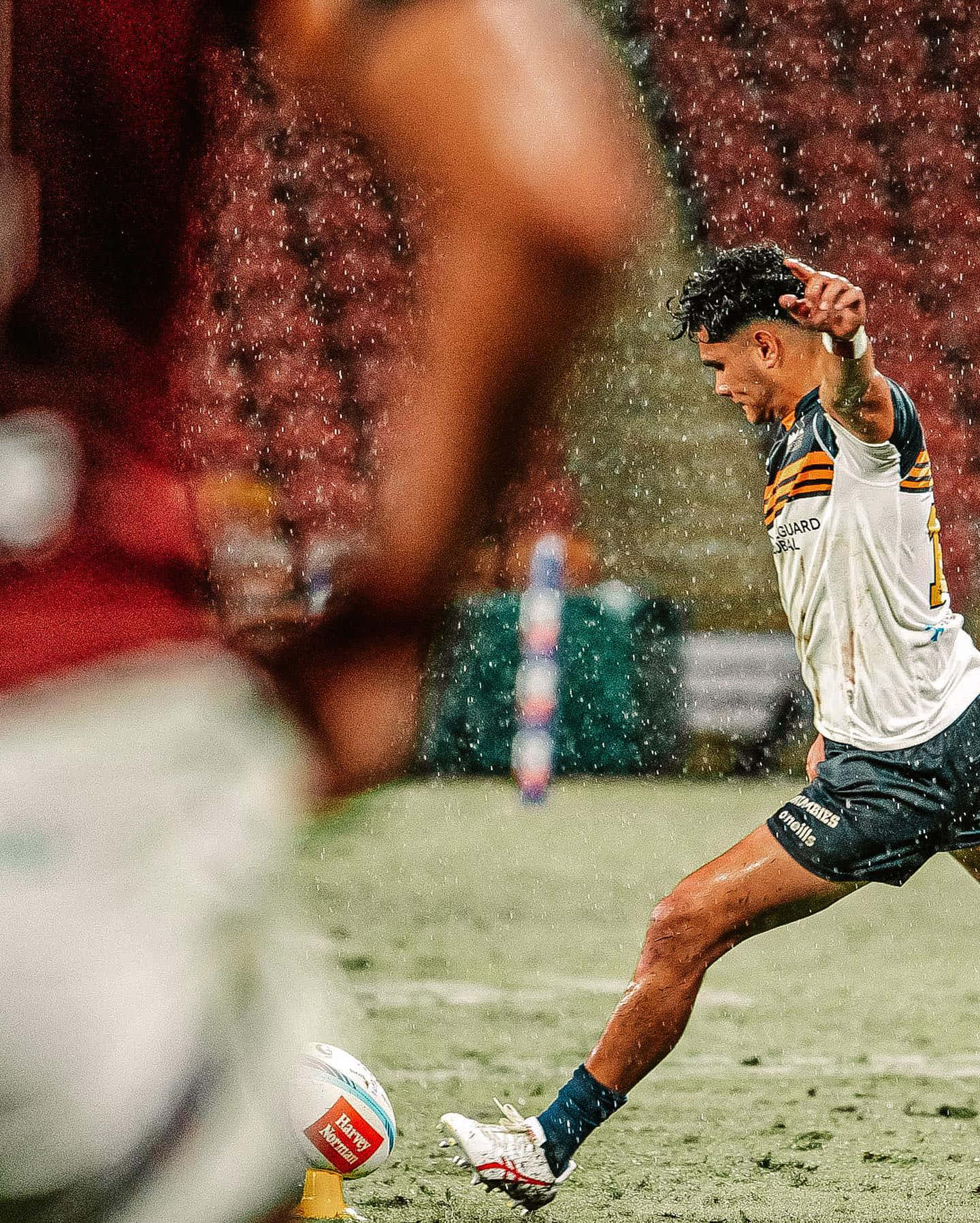 Brumbies 桌布 壁紙 — 一名身穿白色和金色球衣的欖球運動員在傾盆大雨中踢球，空氣中懸浮著水滴。