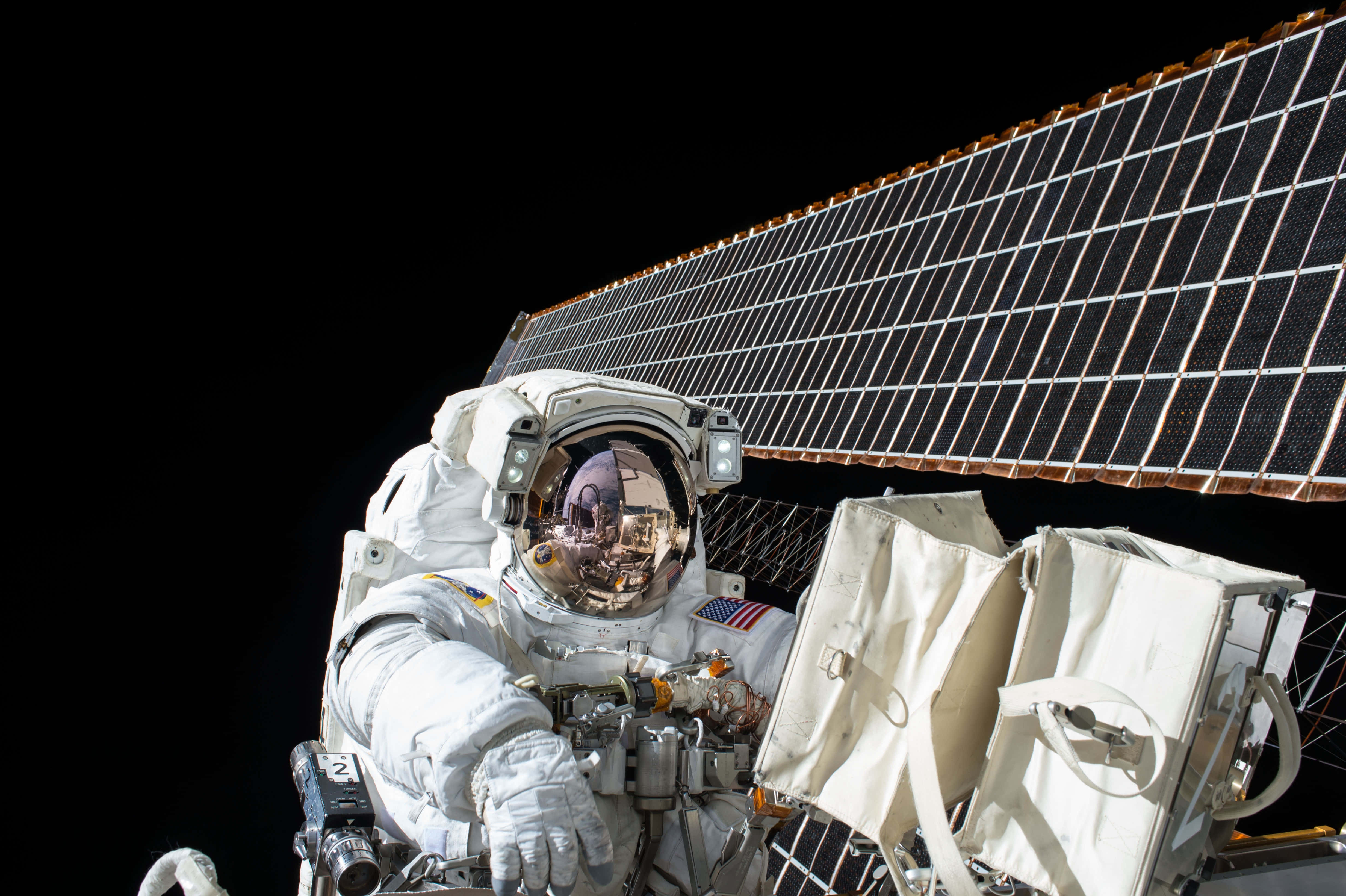 Space Technology 桌布 壁紙 — 一名身穿白色太空衣的太空人在太空船外漂浮，旁邊有太陽能板，背景是漆黑的太空虛空。