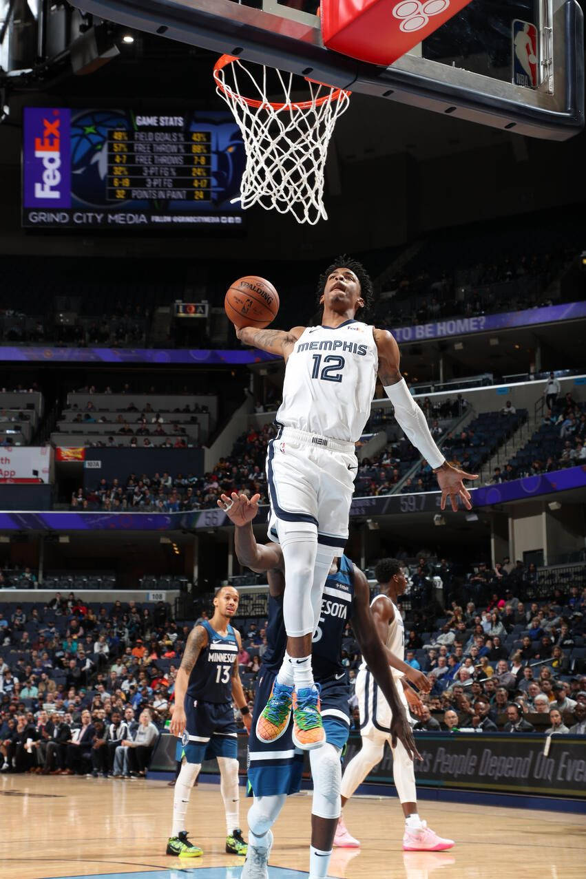 Ja Morant 入樽 桌布 壁紙 — 一名身穿白色孟菲斯球衣的籃球運動員，在對手和座無虛席的場館觀眾注視下，專注地大力入樽。