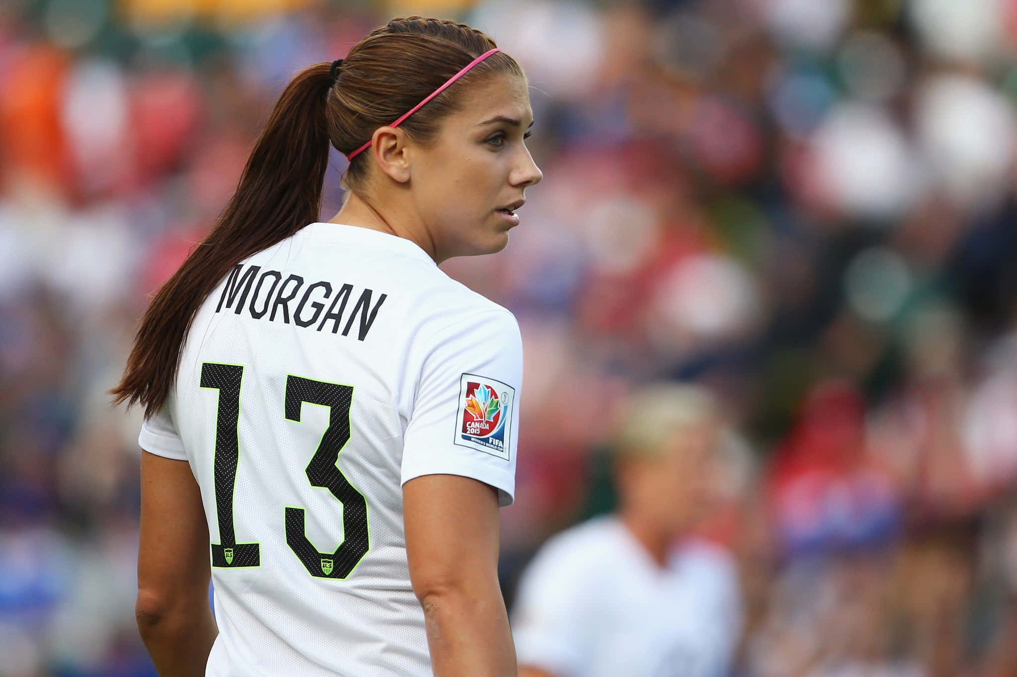 Alex Morgan 桌布 壁紙 — 一名身穿白色球衣、印有摩根名字和13號的女足球員，在日間比賽中專注地站在球場上。