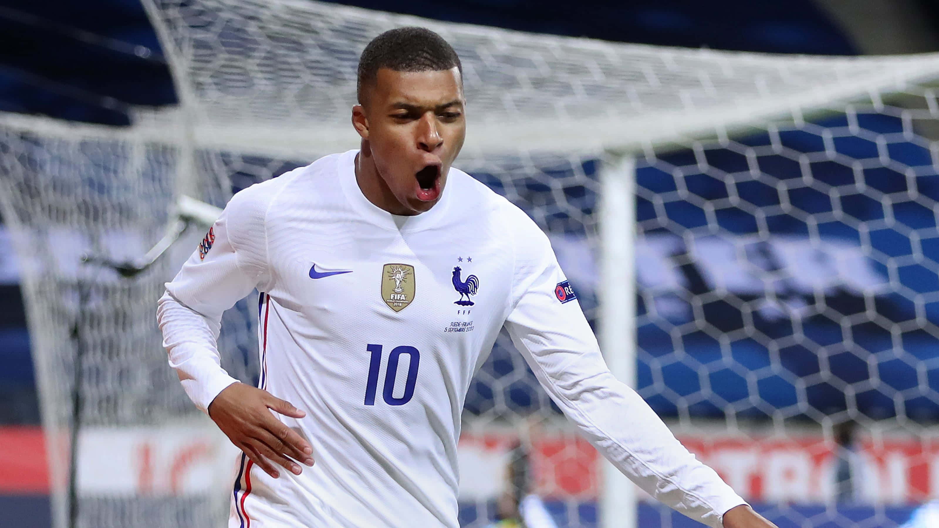 Mbappe 桌布 壁紙 — 一名身穿白色球衣、背號10的法國足球員在球門網前勝利地大喊慶祝入球。