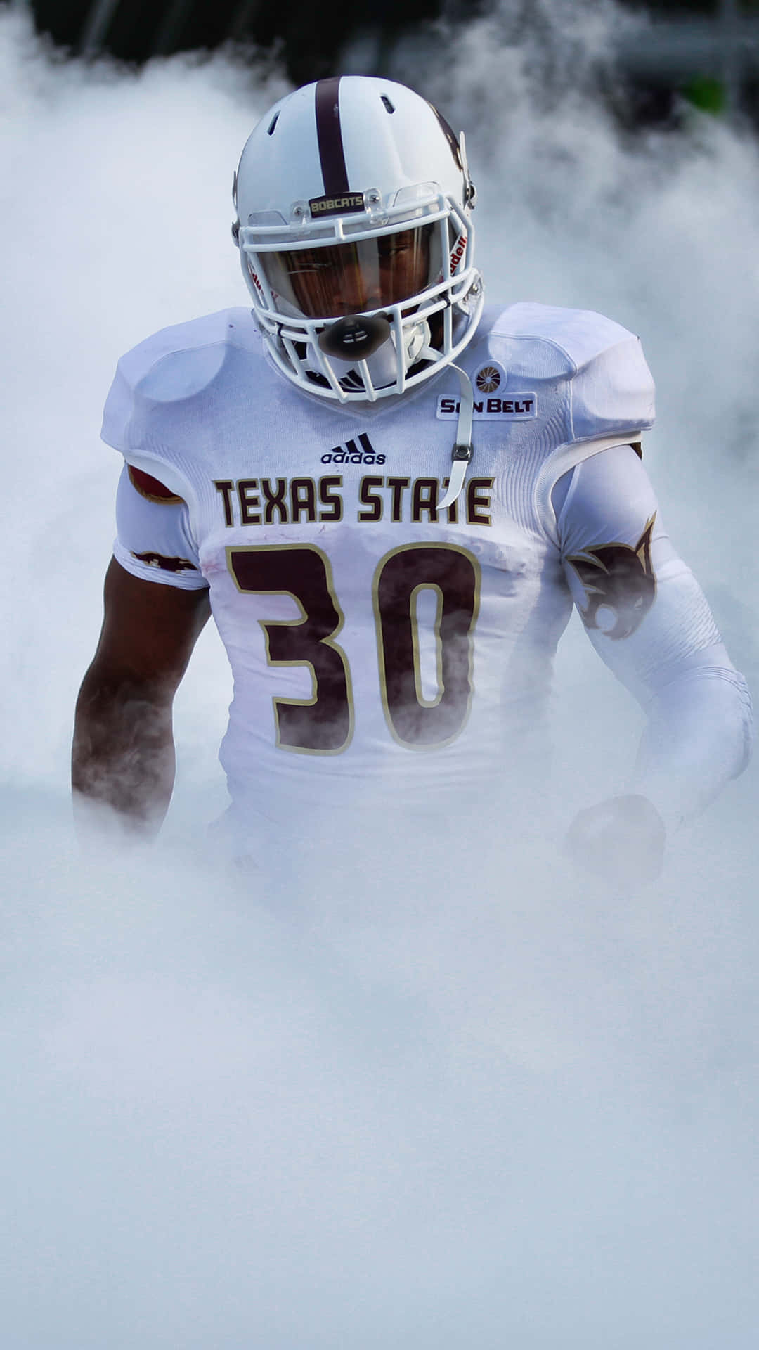 Hook 'em Horns！ 壁紙 — 一名身穿白色球衣的德州州立大學足球員從球場上的濃煙中出現。