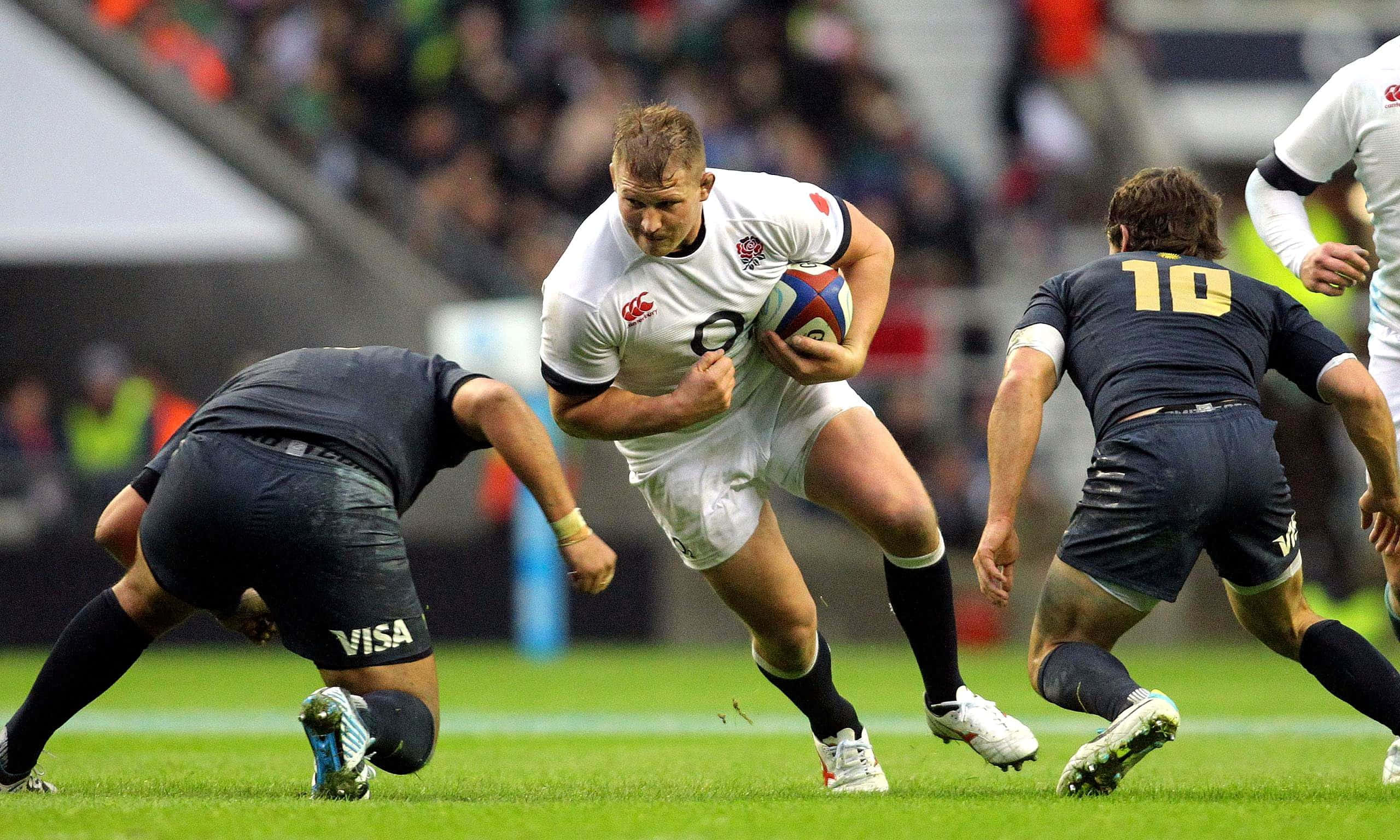 Rugby 桌布 壁紙 — 一名身穿白色球衣的欖球運動員帶球奔跑，身穿深色球衣的對手在充滿活力的綠色場地上攔截他。