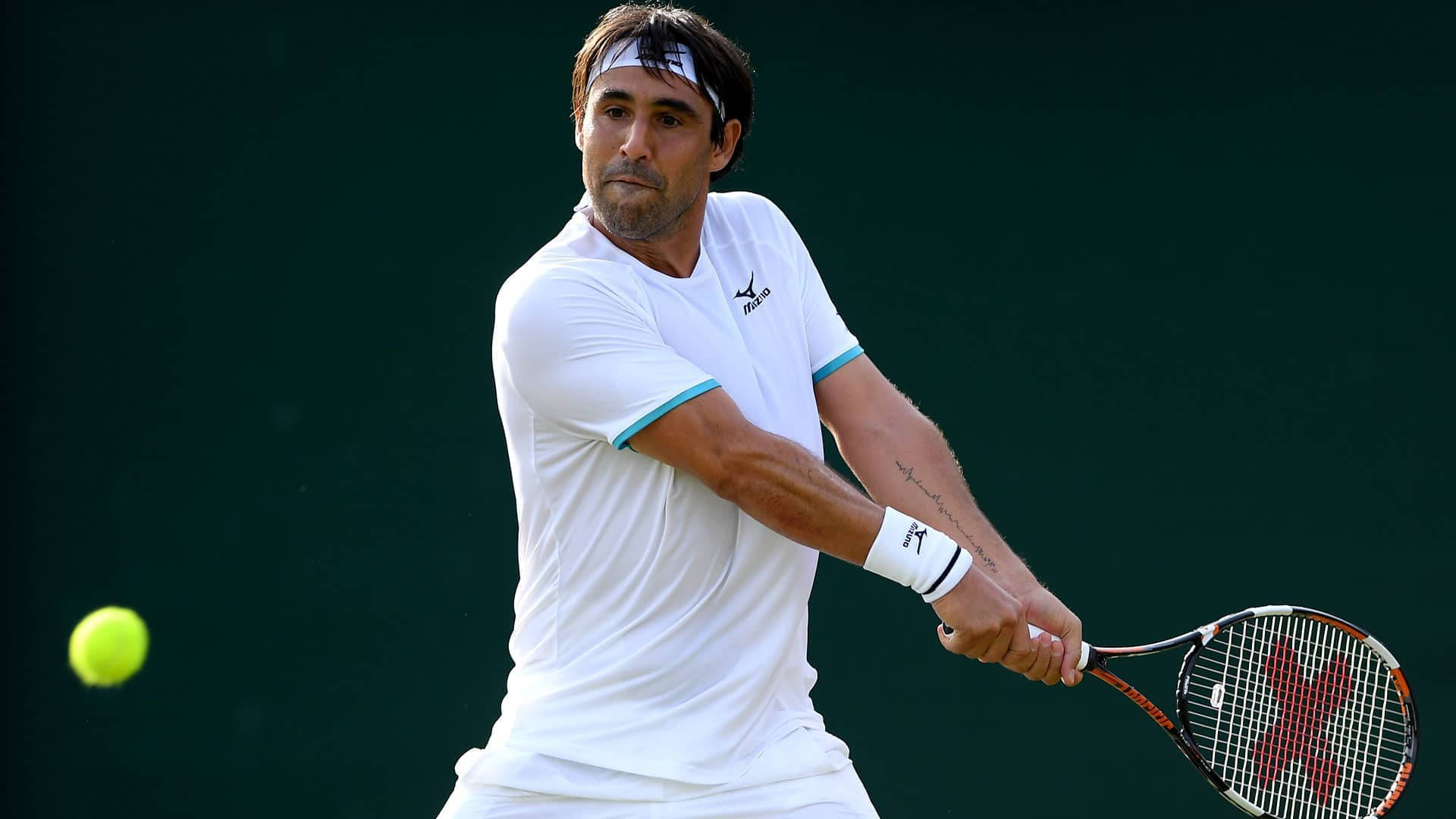 Marcos Baghdatis expertly preparing to counter an incoming ball during a tennis match. 壁紙 — 一名身穿白色球衣的男網球手在深綠色背景下揮拍擊打一個亮黃色的網球。