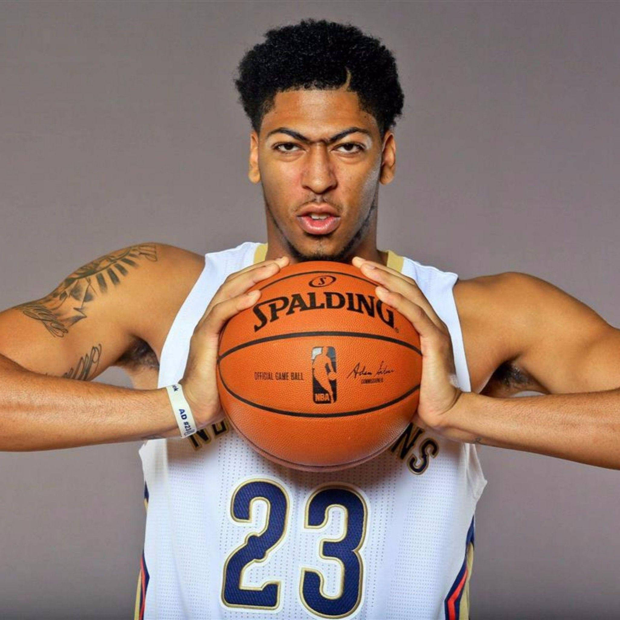 Anthony Davis NBA 壁紙 — 一名身穿白色球衣的籃球運動員，在純灰色背景下，專注地拿著一個橙色的 Spalding NBA 比賽用球。