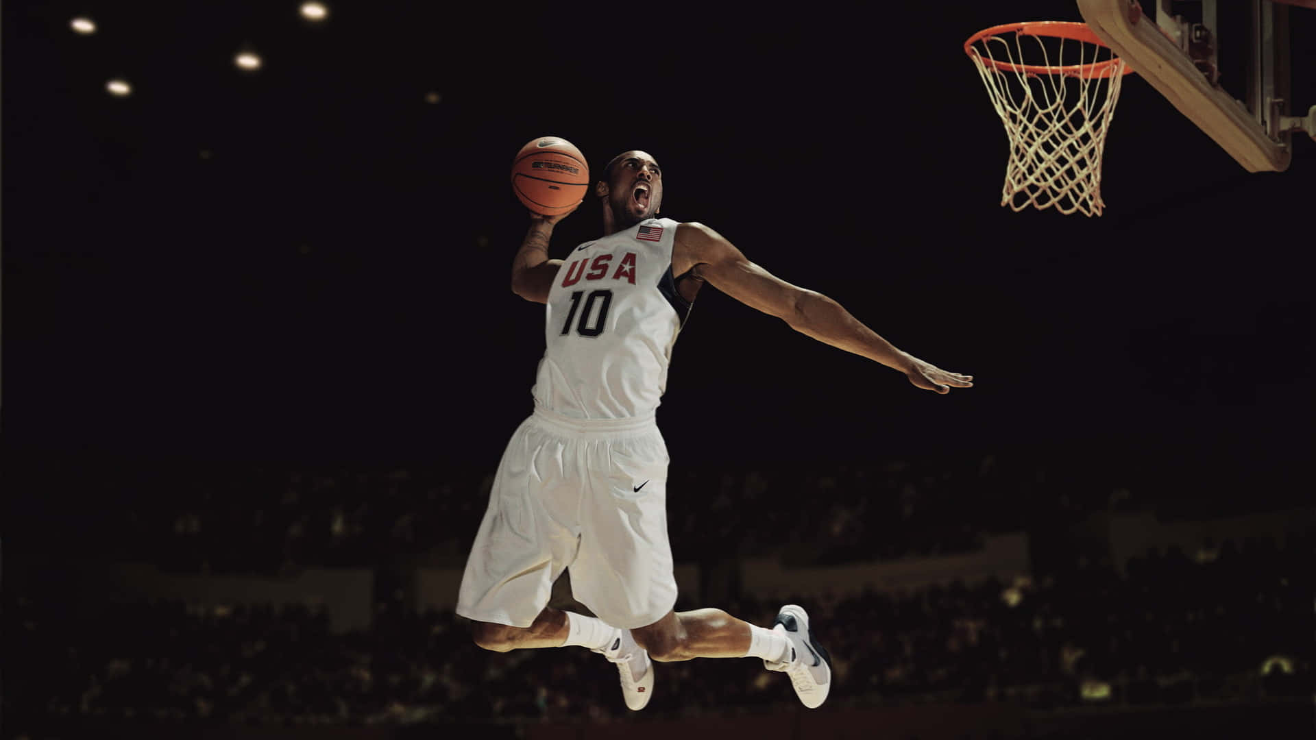 Kobe 桌布 壁紙 — 一名身穿白色美國球衣的籃球運動員在明亮的場館燈光下高高躍起灌籃。