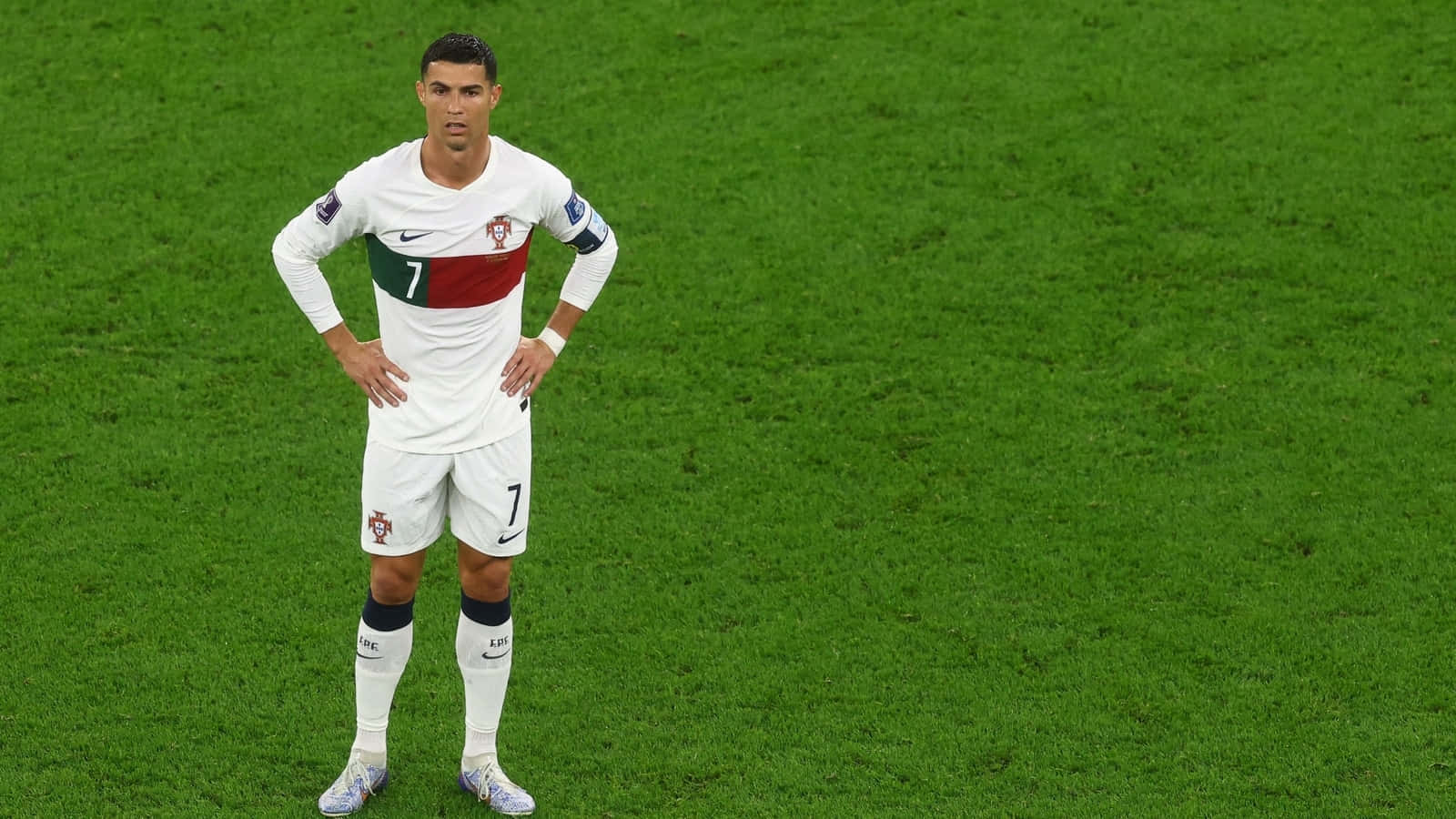 Cristiano Ronaldo 桌布 壁紙 — 一名身穿白色葡萄牙7號球衣的足球員獨自站在充滿活力的綠色球場上，雙手叉腰。