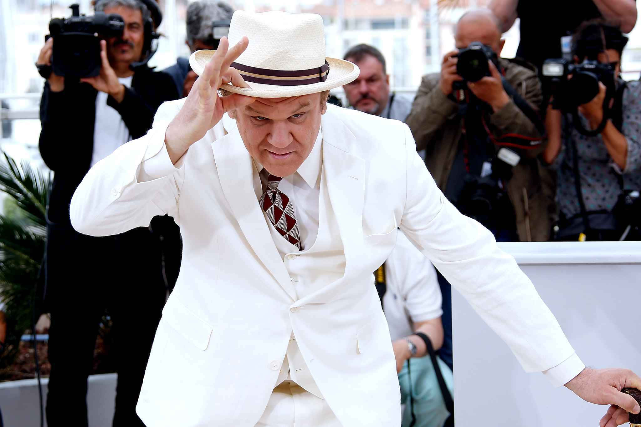 John C. Reilly 桌布 壁紙 — 一名身穿白色西裝和軟呢帽的男子在紅地毯活動中被攝影師包圍，調整他的帽子。