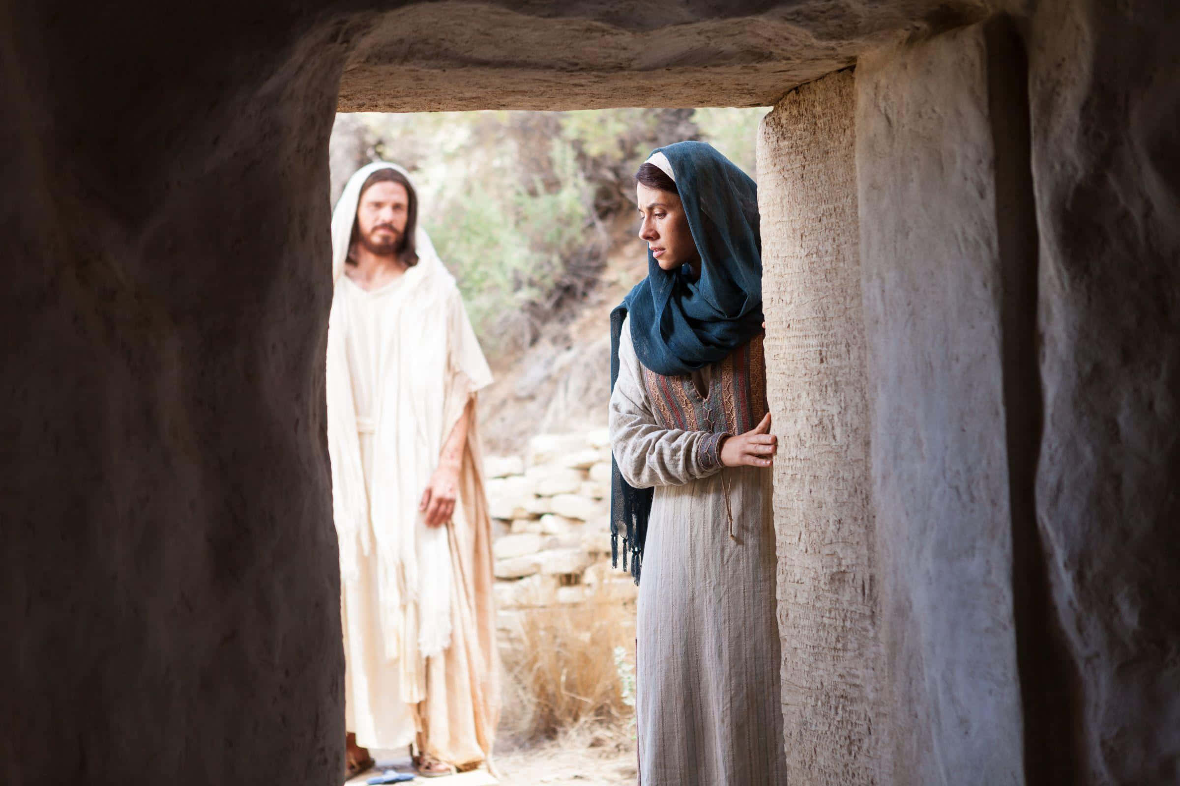 Mary Magdalene 桌布 壁紙 — 一名身穿白色長袍的男子站在石門中，一名戴著藍色頭巾的女子緊握著她旁邊的柱子。