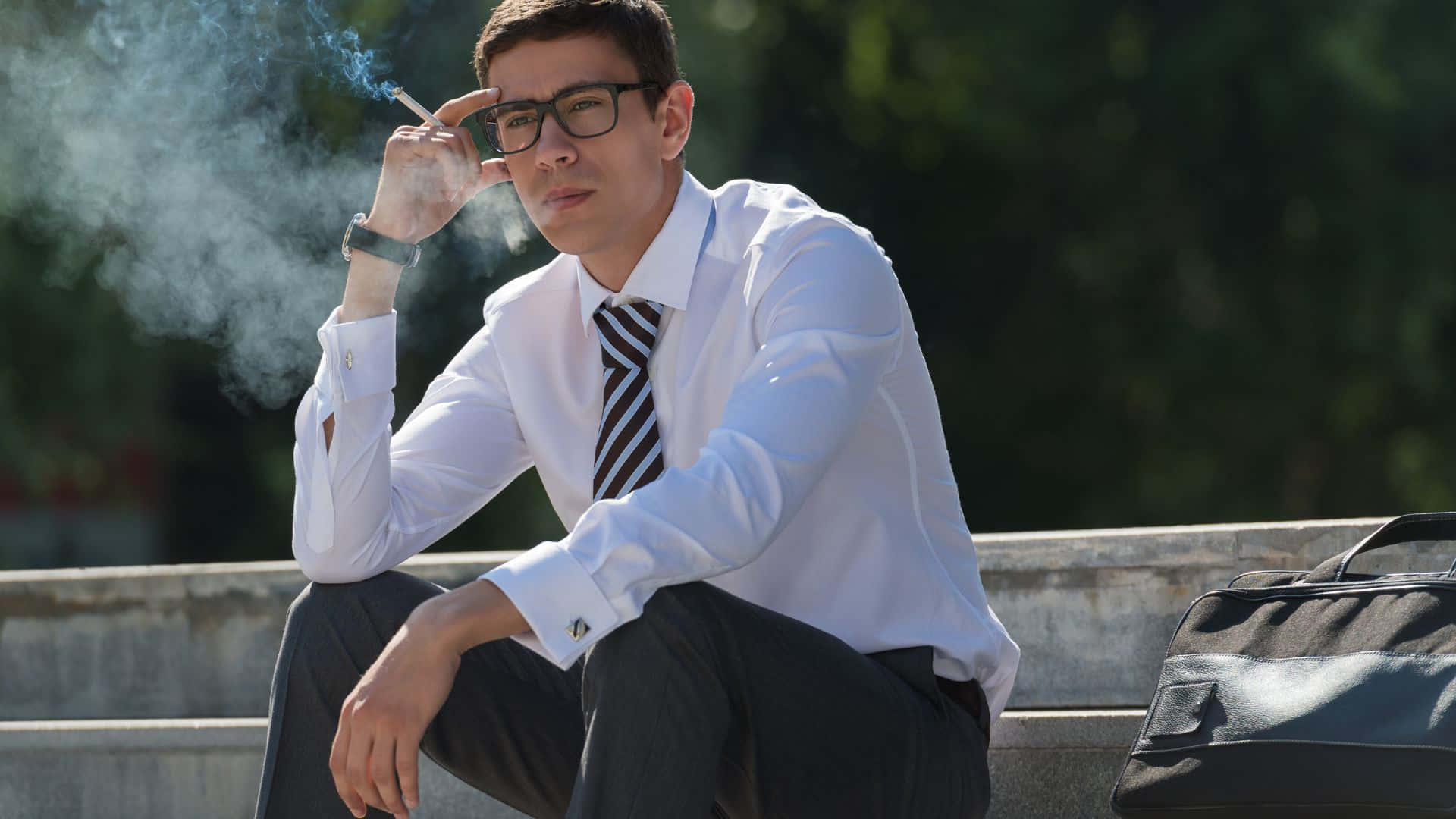 吸煙 桌布 壁紙 — 一名身穿白襯衫、戴眼鏡的年輕男子坐在戶外的混凝土台階上抽煙。