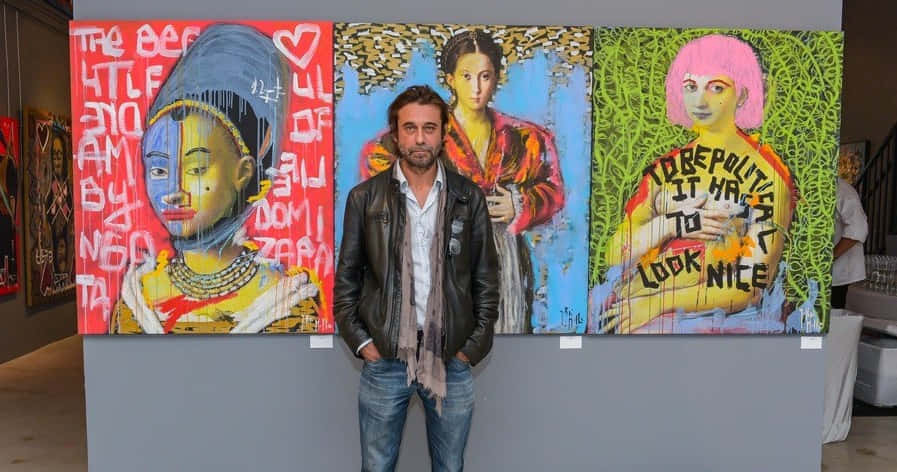 Jordi Mollà 桌布 壁紙 — 一名身穿皮褸的男子站在畫廊中三幅充滿活力、充滿文字的普普藝術畫作前。