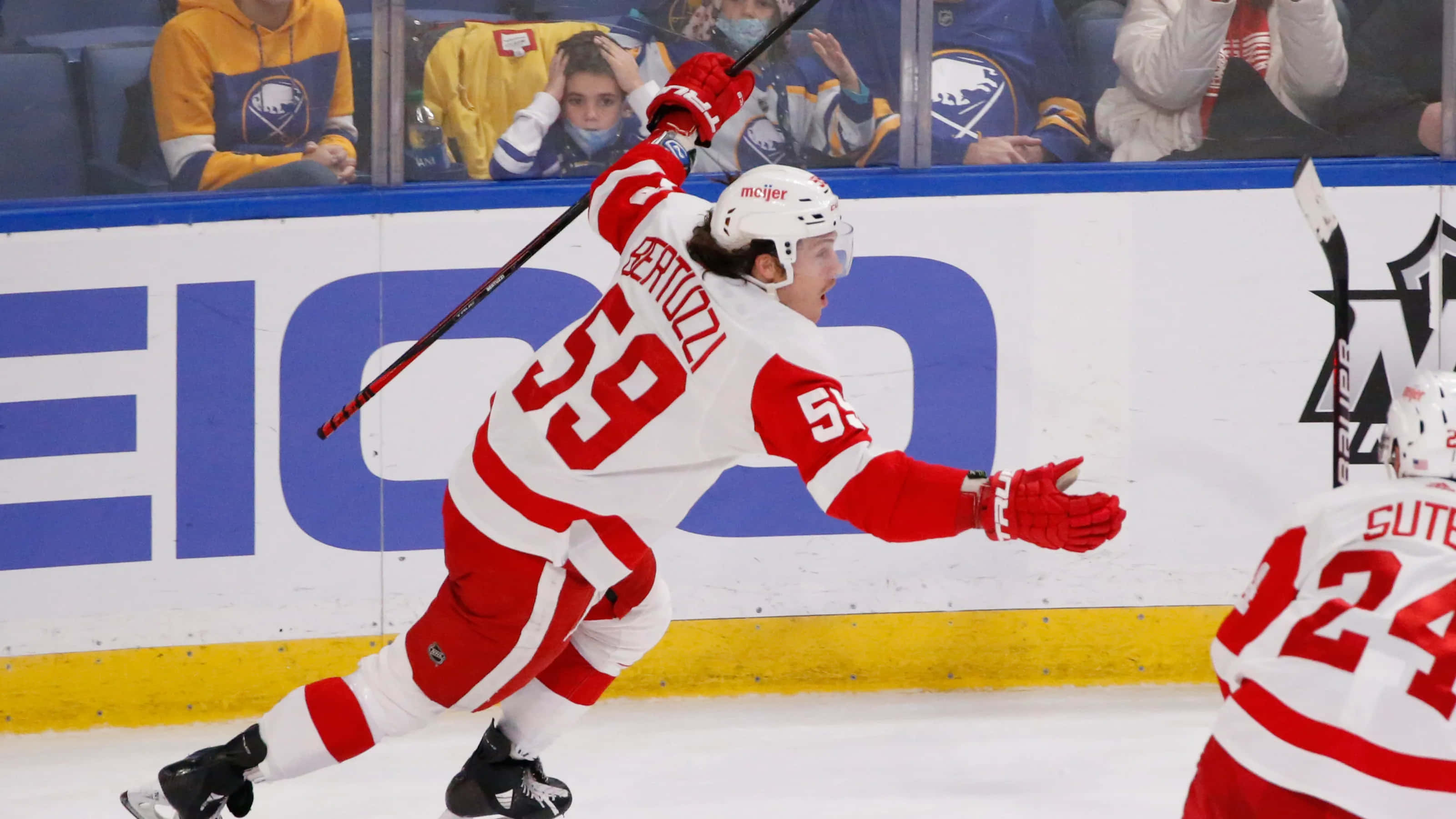 Tyler Bertuzzi 桌布 壁紙 — 一名身穿紅白球衣的曲棍球運動員在冰上高舉雙臂和球棍慶祝入球。