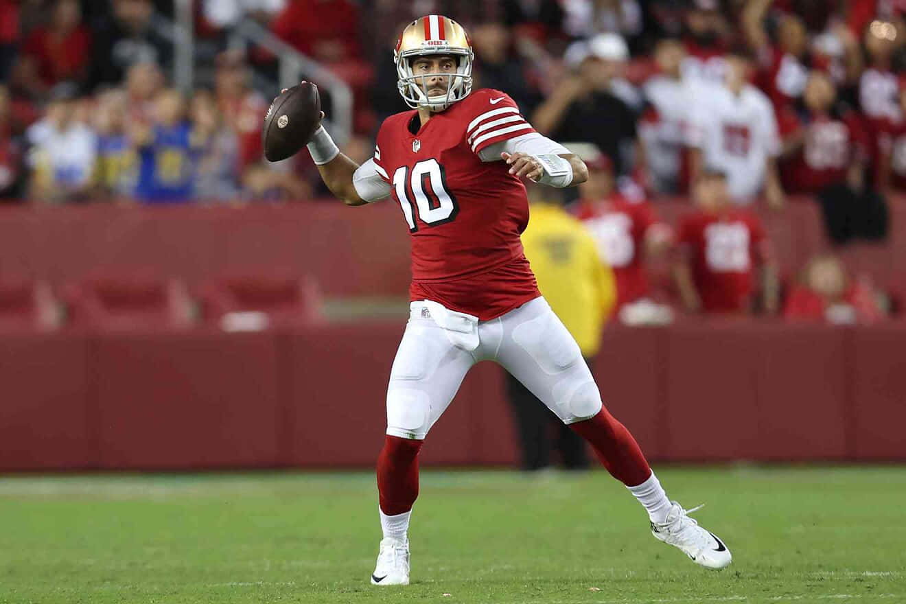 Jimmy Garoppolo 桌布 壁紙 — 一名身穿紅白球衣的美式足球四分衛在綠色球場上擲球，背景是模糊的體育場人群。