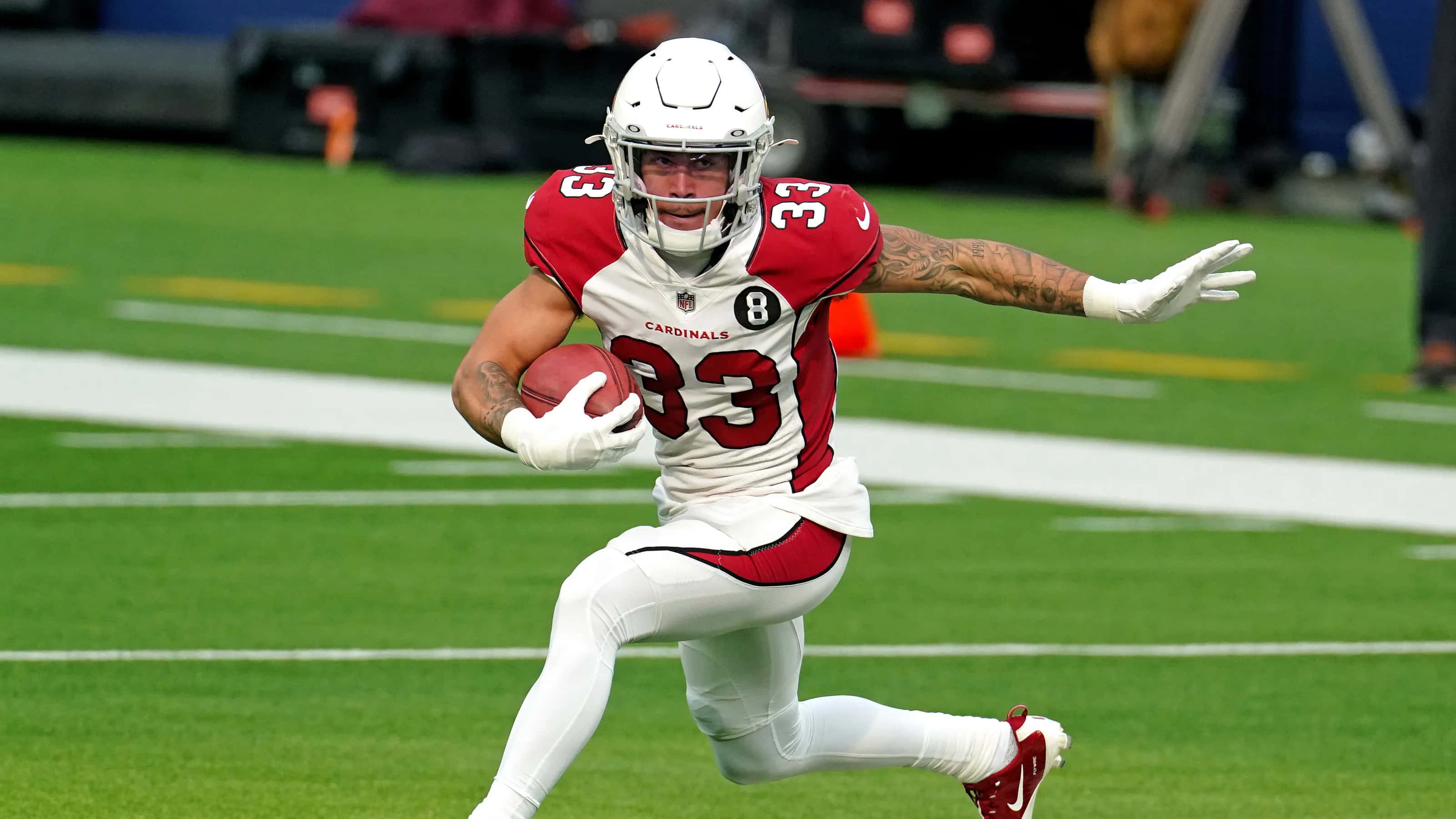Byron Murphy 桌布 壁紙 — 一名身穿紅白球衣的足球員，手持足球在綠色球場上飛奔。