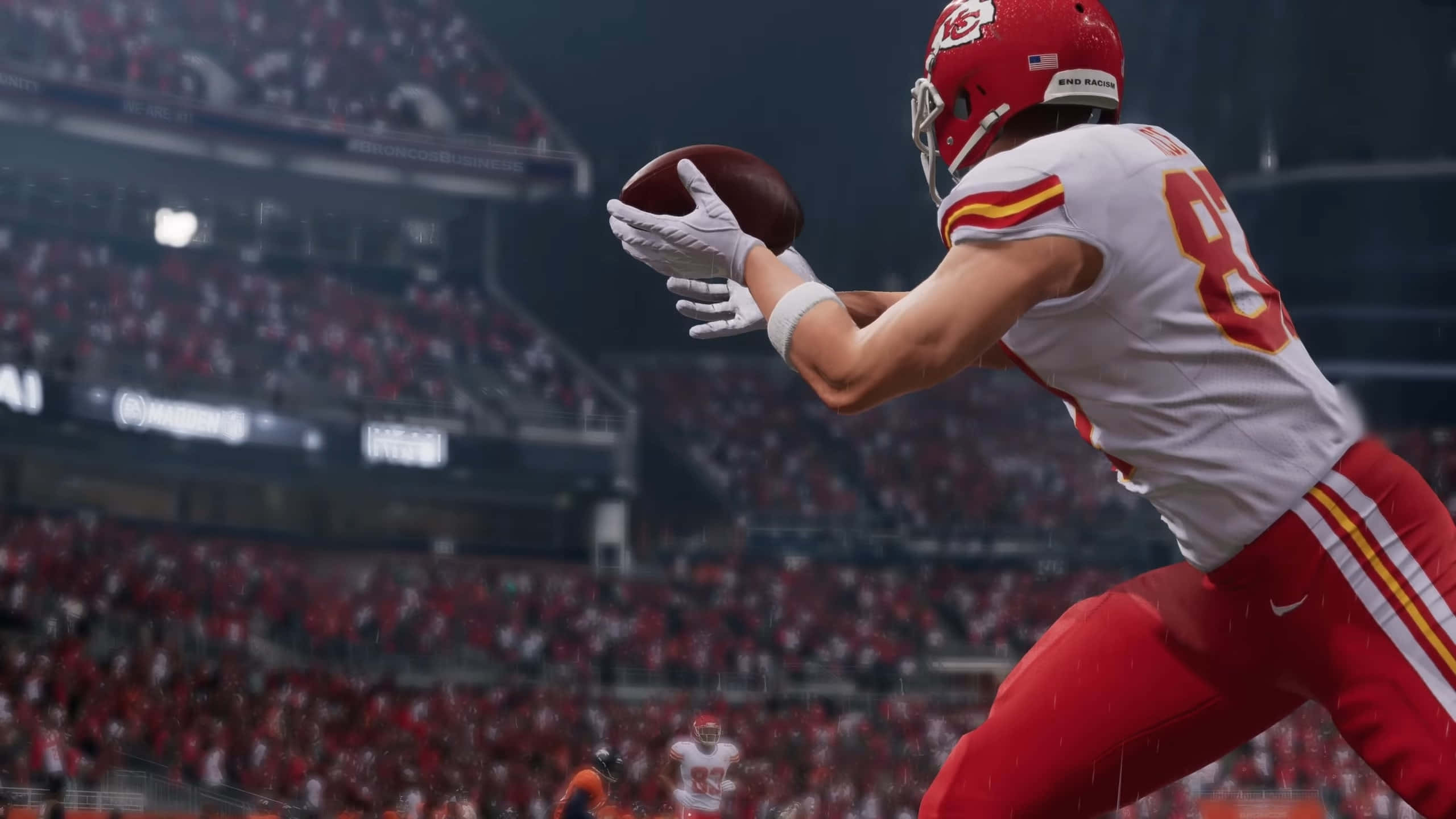 Madden NFL 22 桌布 壁紙 — 一名身穿紅白球衣的足球運動員在擠滿觀眾的體育場內，在明亮的燈光下空中接球。