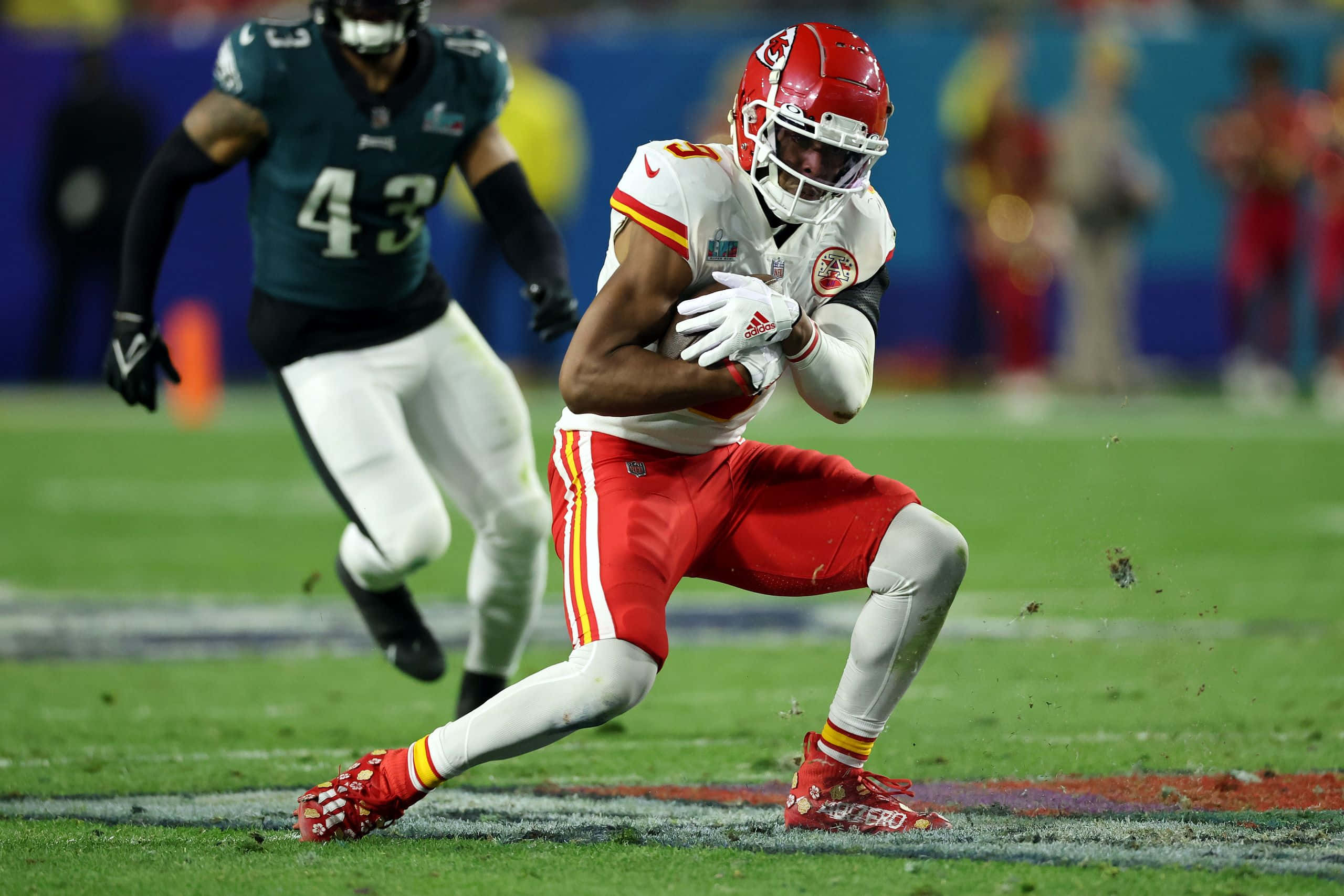 Juju Smith Schuster 桌布 壁紙 — 一名身穿紅白裝備的堪薩斯城酋長隊美式足球員持球衝刺，而費城老鷹隊的防守球員在充滿活力的綠色球場上追趕他。
